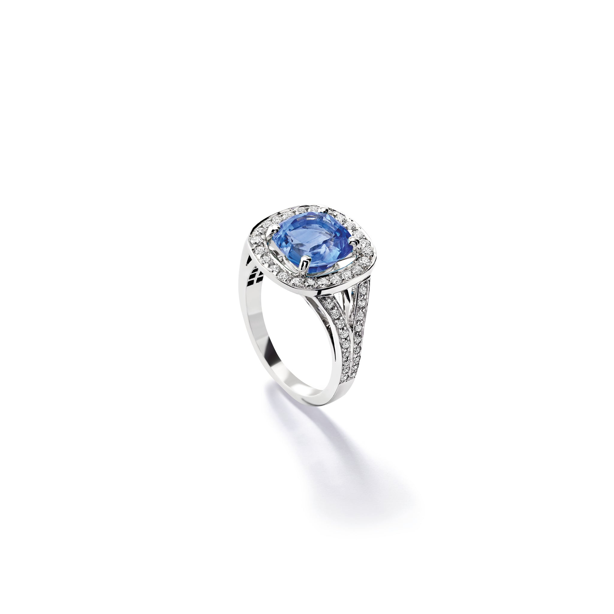 Handcrafted 18ct white gold engagement ring featuring a large, cushion-cut dark blue tanzanite surrounded by a halo of small diamonds and smaller diamonds embedded along the band.