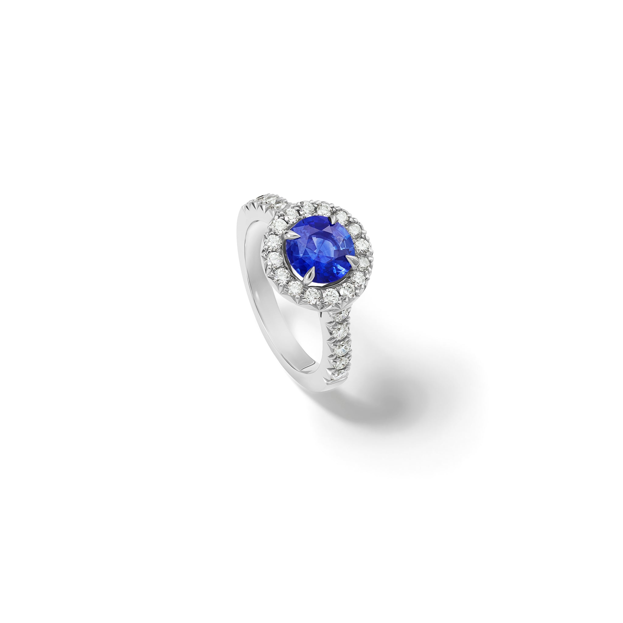 Handcrafted platinum engagement ring with a round sapphire at the centre, surrounded by smaller diamonds. The band of the engagement ring is also set with small diamonds.