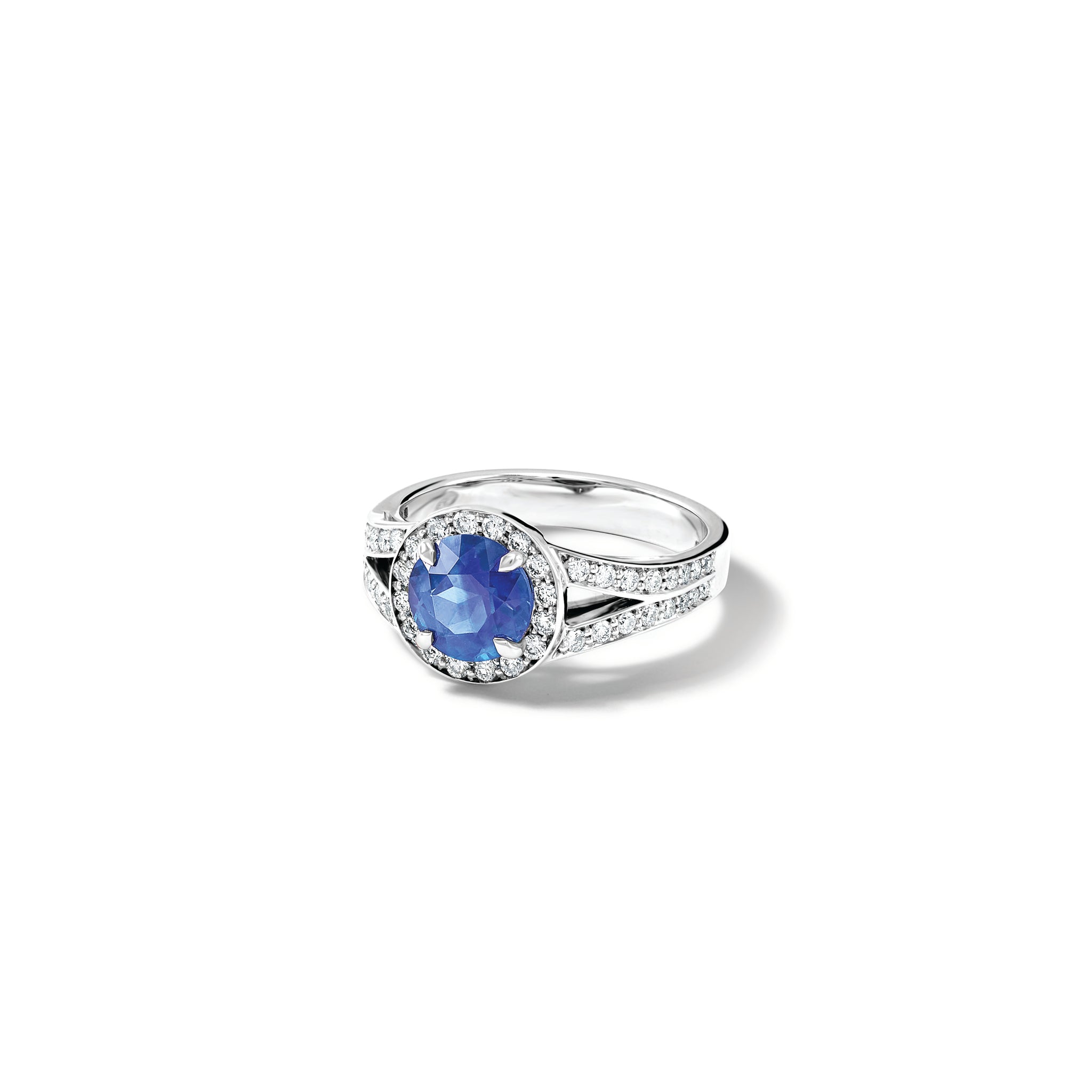 Handcrafted 18ct white gold engagement ring with a large round central sapphire surrounded by a halo of small diamonds and smaller diamonds embedded along the band.