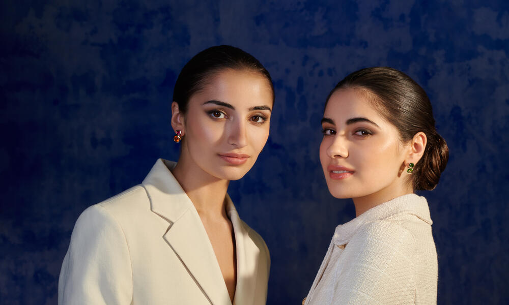 Two models wearing handcrafted yellow gold earrings featuring two square shaped gemstones in vibrant colours, inspired by China.