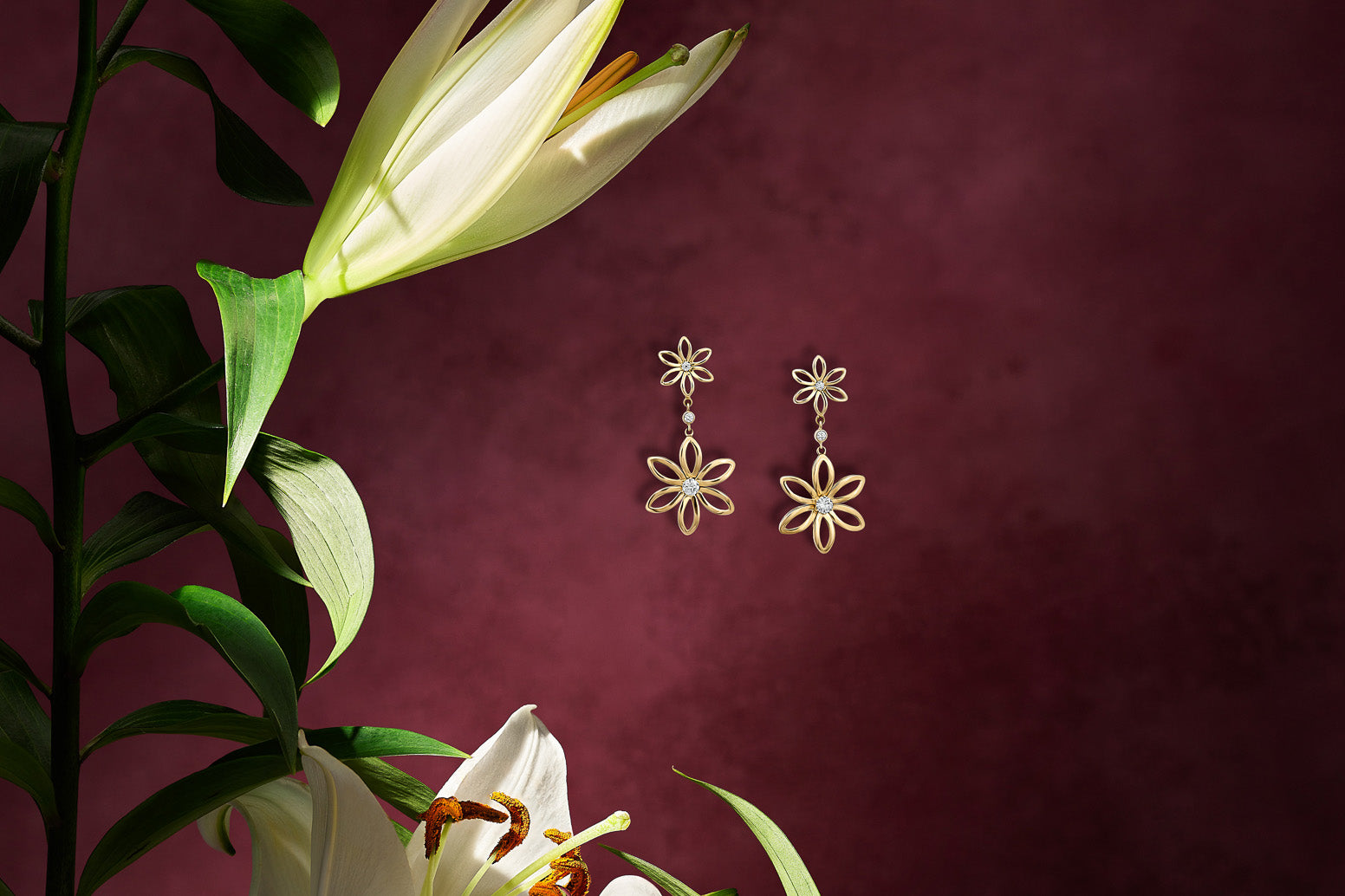 Handcrafted yellow gold earrings with two fleur de lys flower shapes with diamonds at the centre.