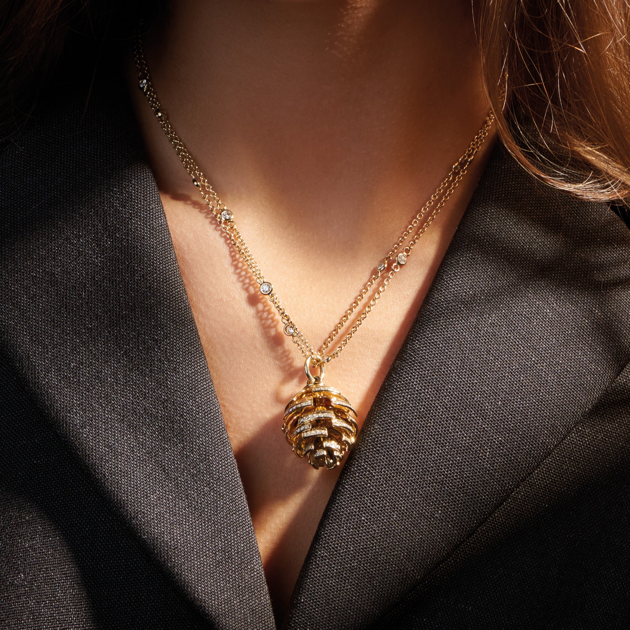 Model wearing a handcrafted yellow gold fir cone shaped necklace pendant with diamond pav�.