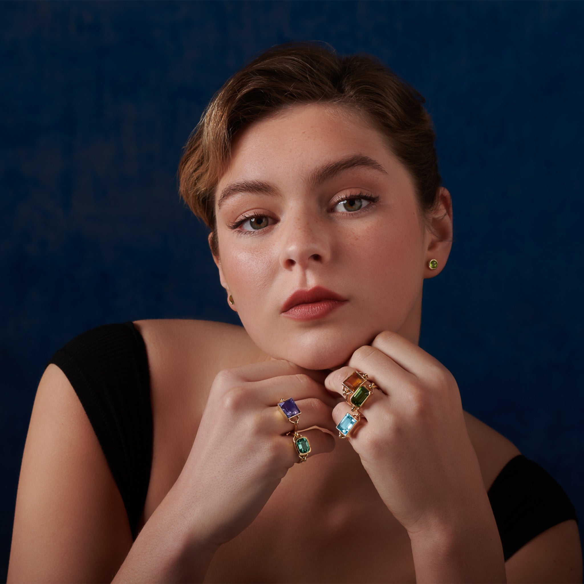 Model wearing handcrafted rings in precious metals featuring central precious stones.