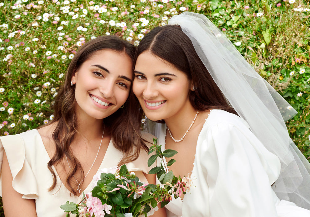 A bride and her bridesmaid sitting together, both elegantly adorned in pearl and diamond jewellery.