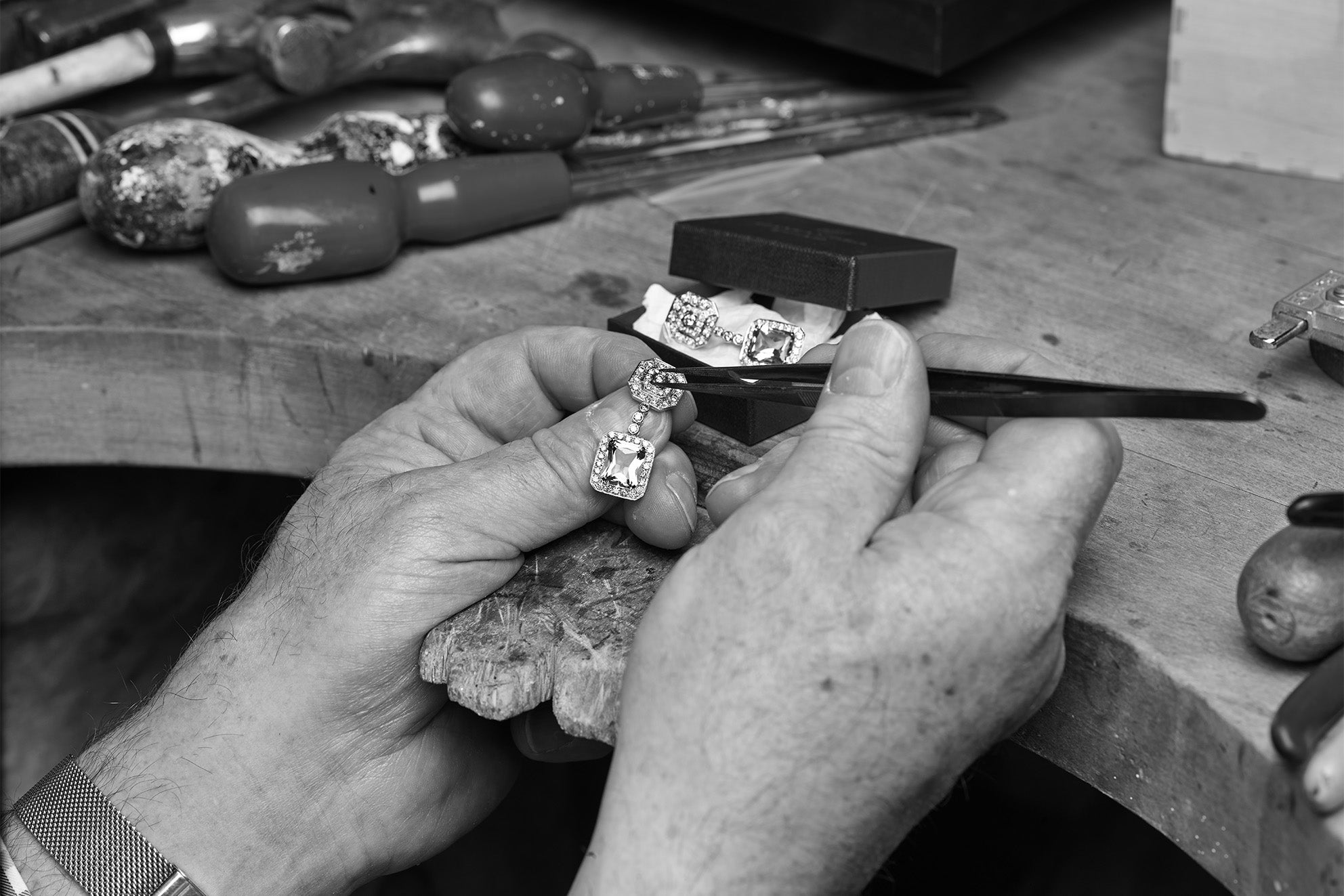 A craftsman working on a pair of handcrafted earrings, which are adorned with precious stones and made from precious metal.