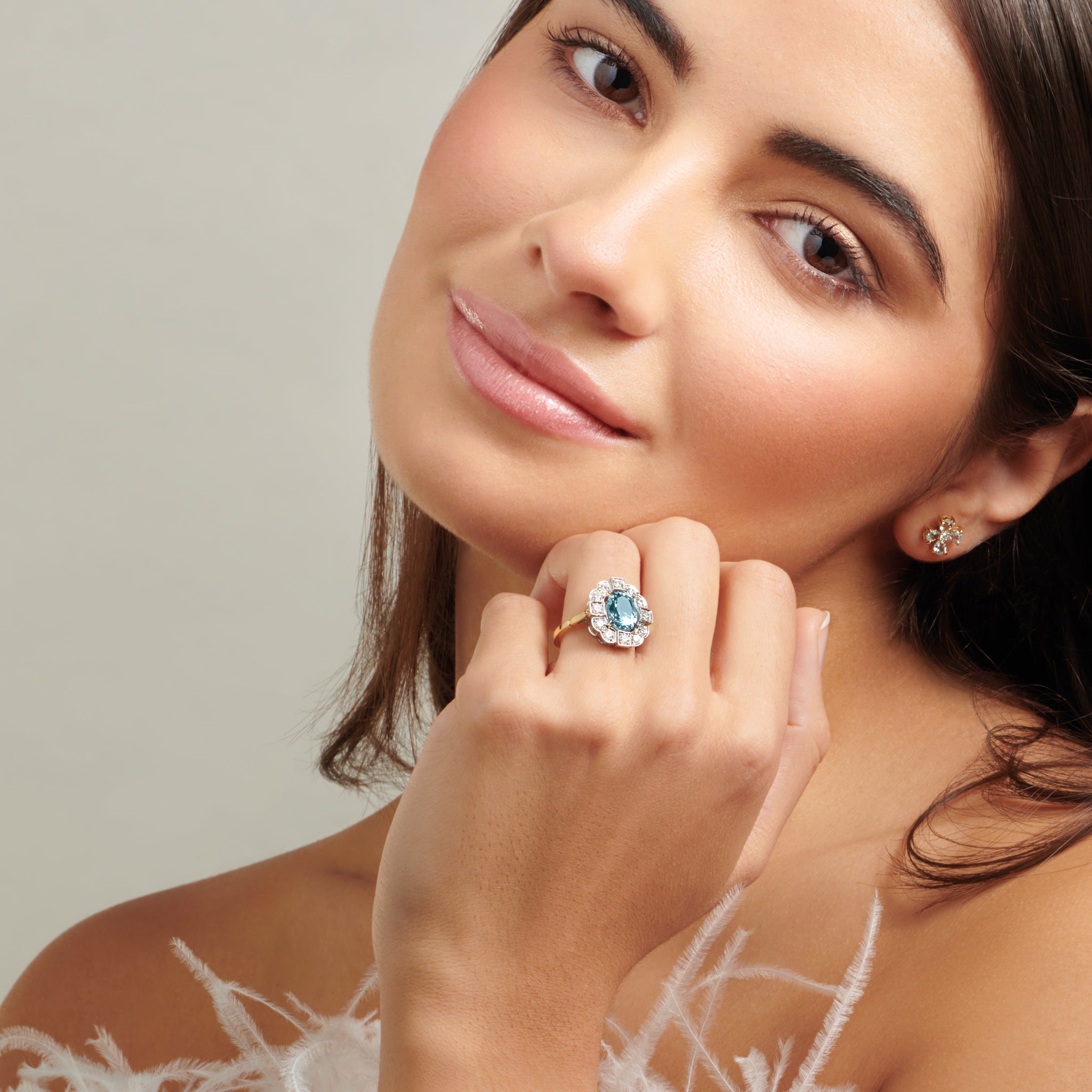 Model wearing a handcrafted engagement ring featuring a central oval aquamarine, surrounded by a halo of small diamonds. The diamonds are set in a 18ct white gold while the band is 18ct yellow gold.