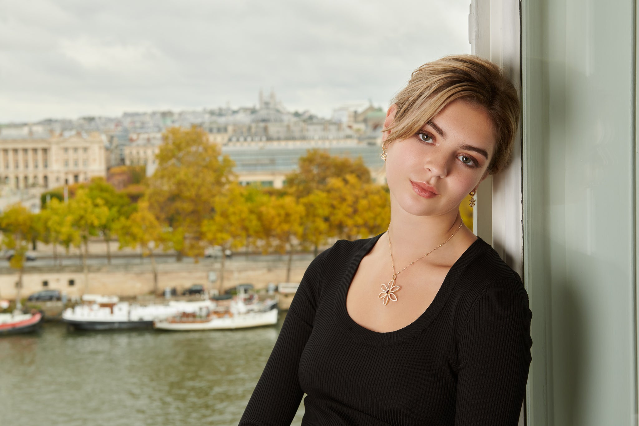 Model wearing a handcrafted floral shaped yellow gold necklace pendant featuring a red garnet at the centre.