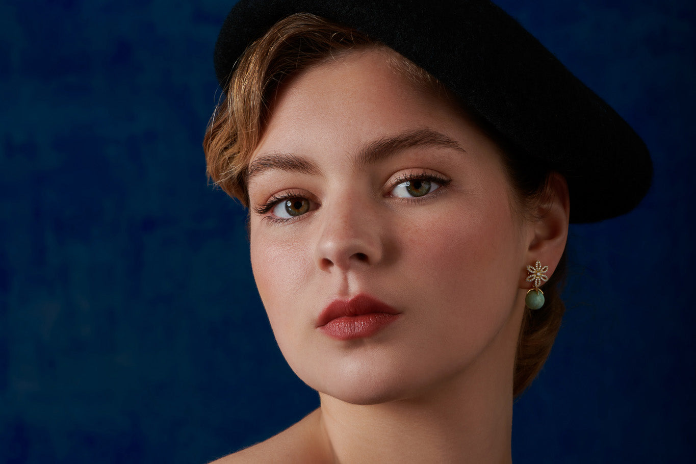 Model wearing handcrafted yellow gold earring drops featuring emerald pendants, birthstone of May.