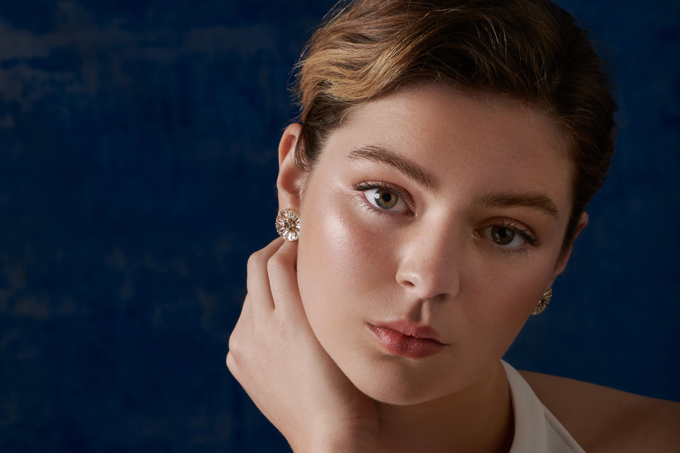 Model wearing handcrafted yellow gold earring halos featuring a circular shape of precious stones with an interchangeable central stud earring.