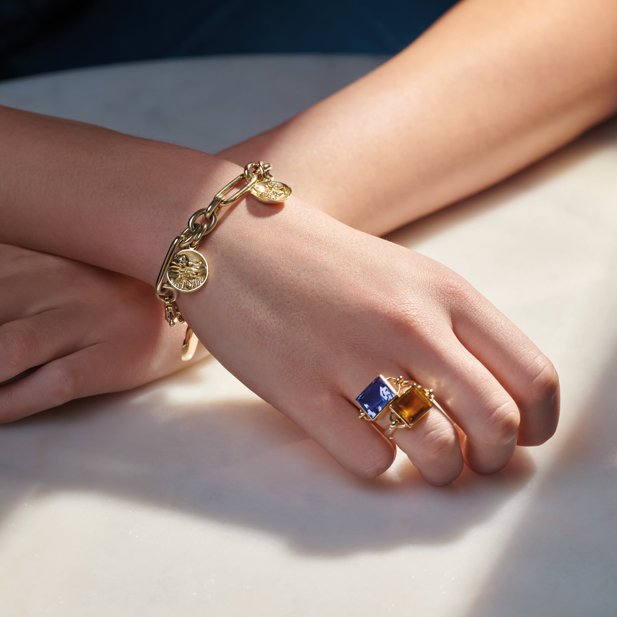 Model wearing a handcrafted yellow gold charm bracelet featuring five gold charms 'en relief' with culture from France. 