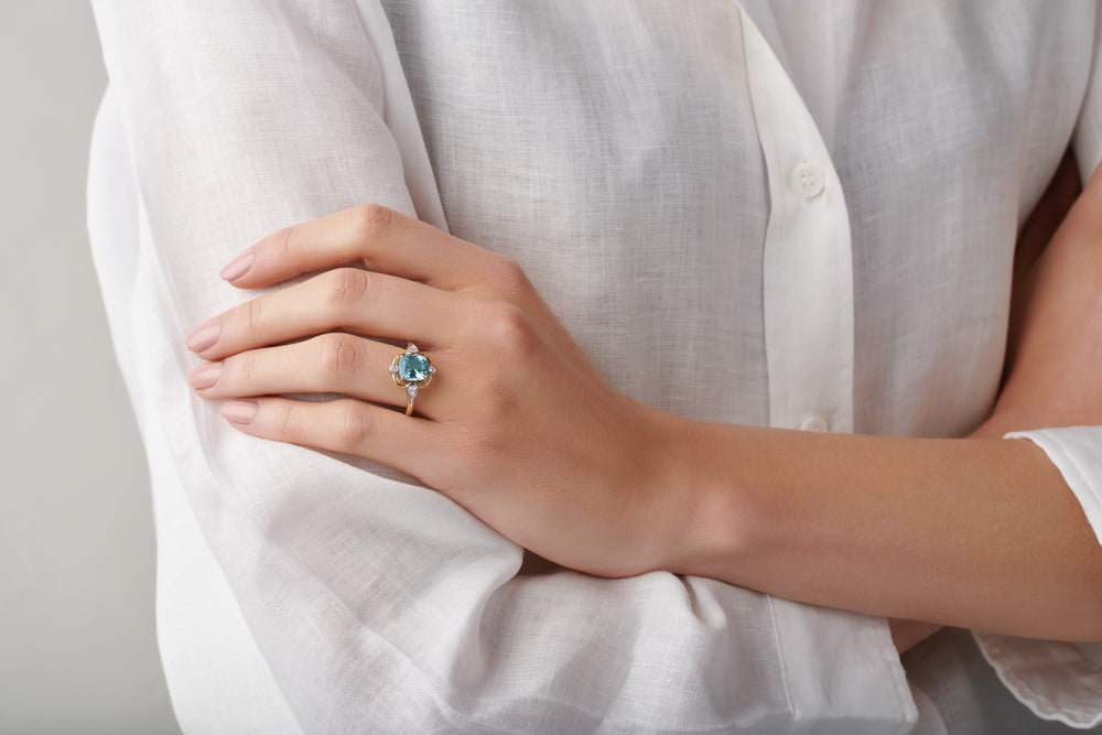 Model wearing a handcrafted yellow gold ring featuring a facetted aquamarine, birthstone of March.