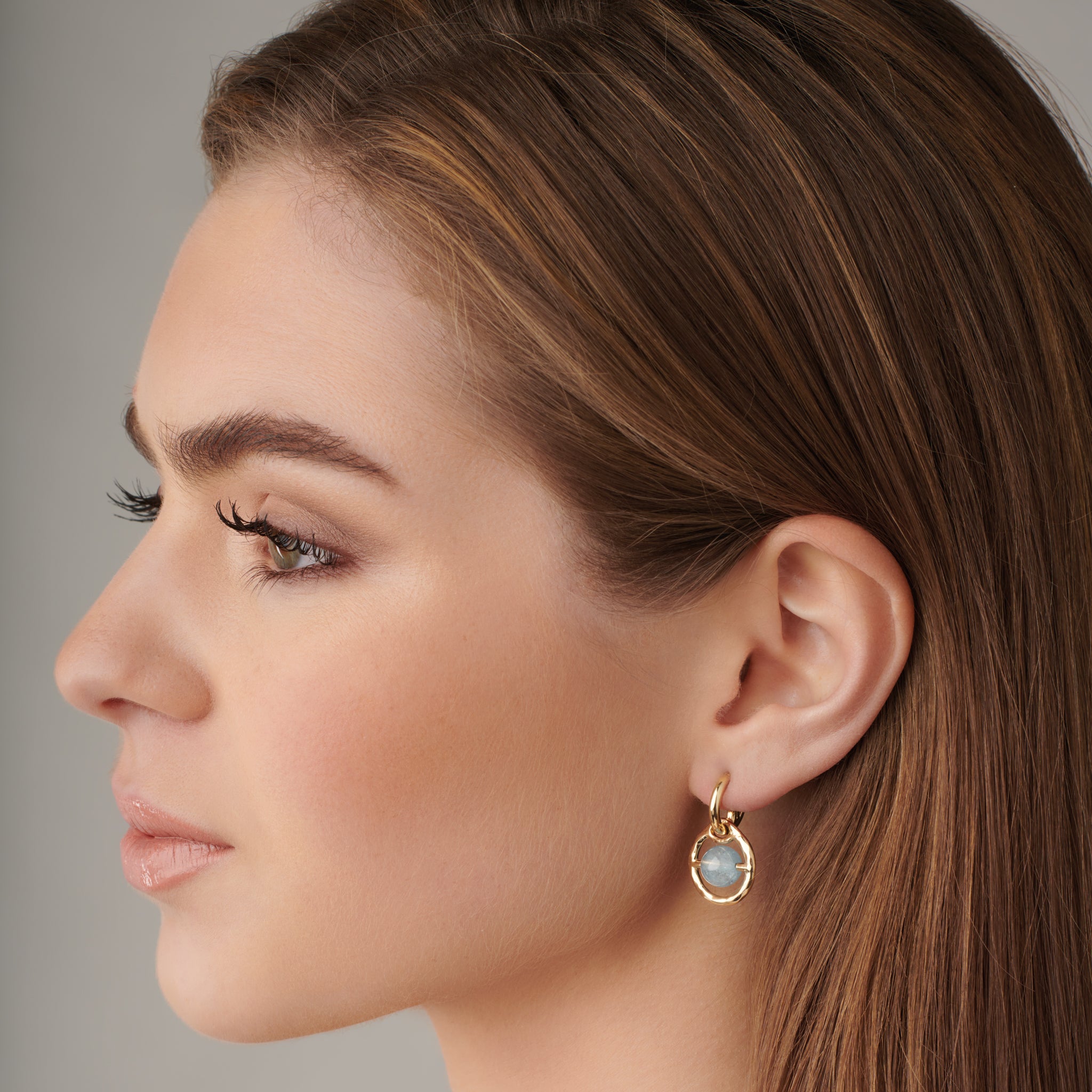 Model wearing handcrafted earring drops in precious metal featuring a round precious stone held within a circle.