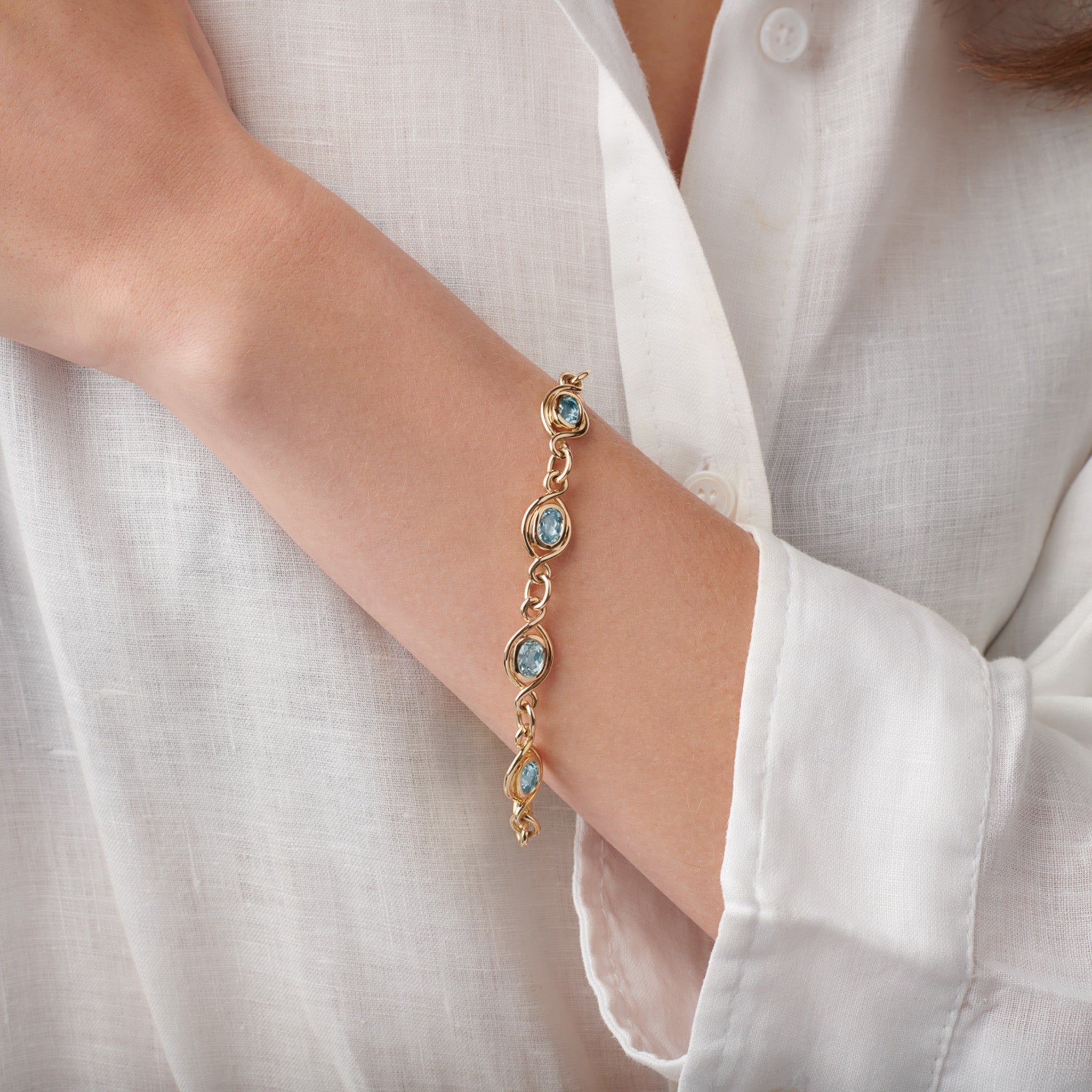 Model wearing a handcrafted yellow gold bracelet with eight aquamarine gemstones, birthstone of March.