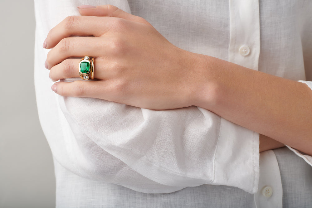 Model wearing a handcrafted yellow gold ring featuring a facetted emerald, birthstone of May.