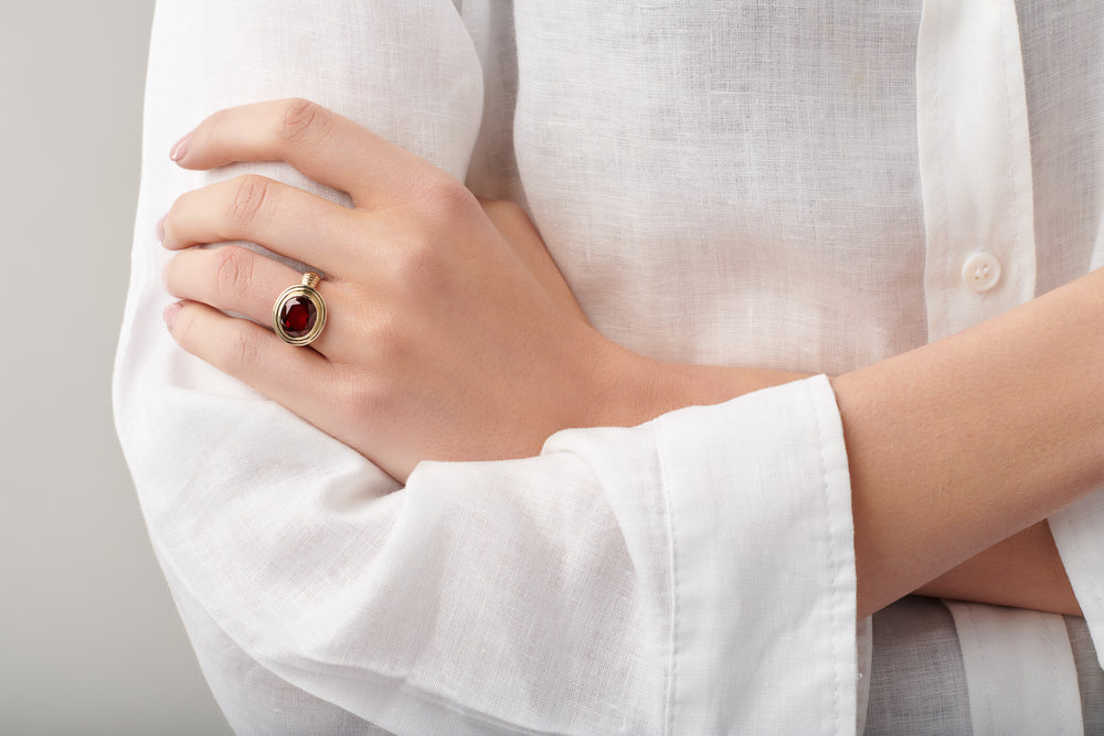 Model wearing a handcrafted yellow gold ring featuring a facetted garnet, birthstone of January.