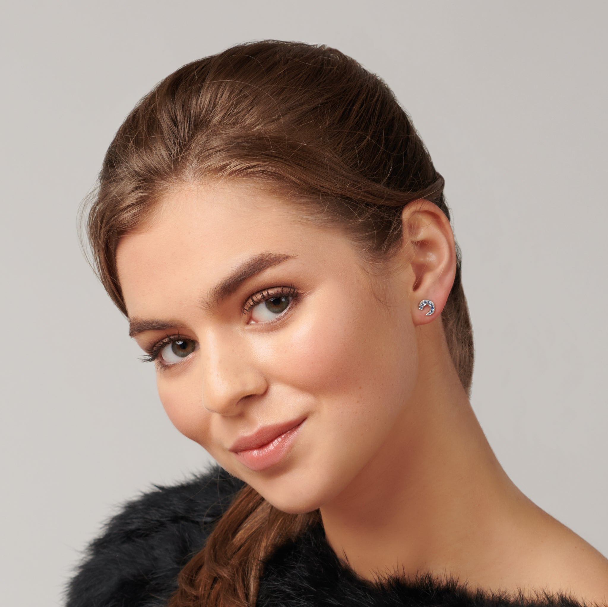 Model wearing handcrafted stud earrings in precious metal featuring a crescent shape with precious stone pavé.