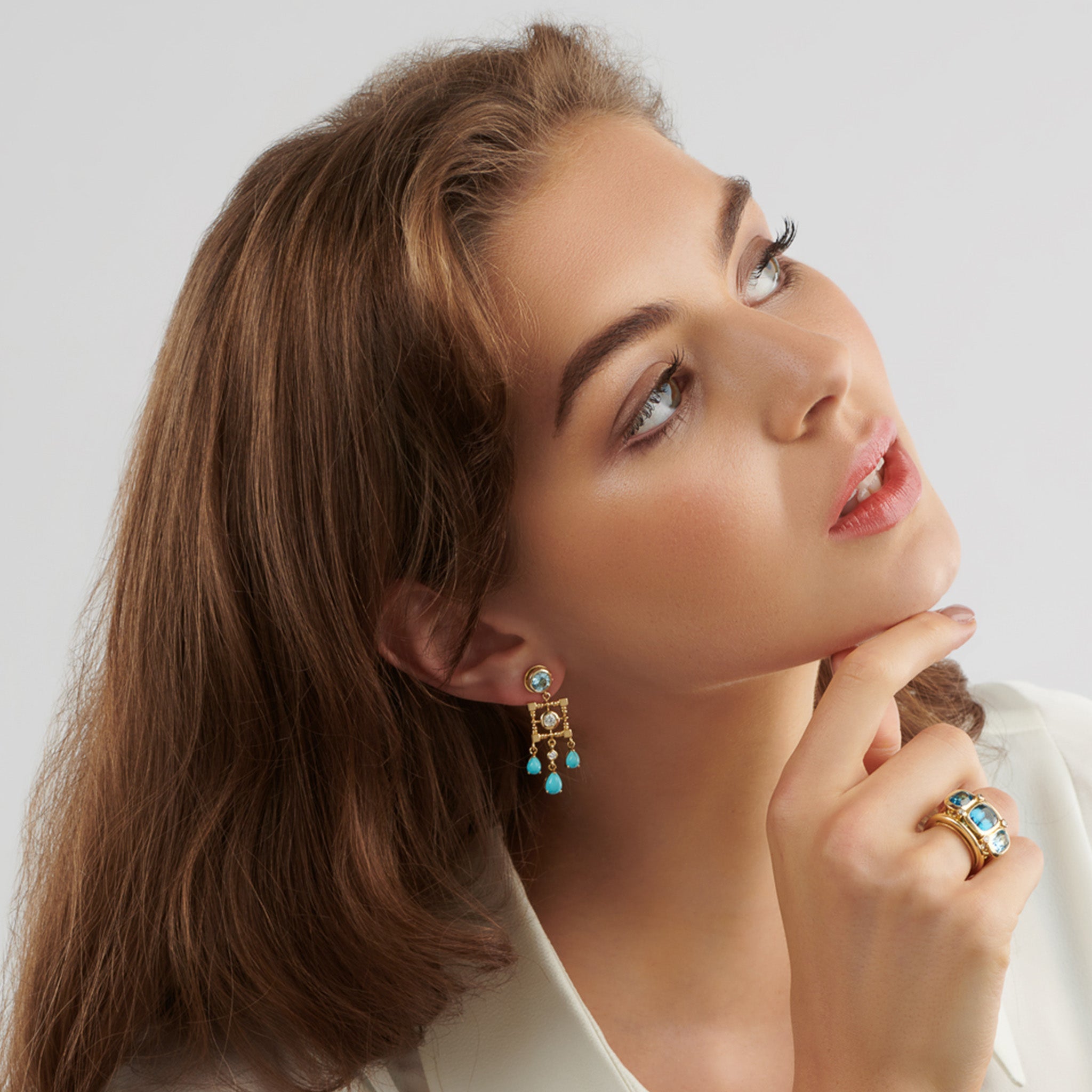 Model wearing handcrafted yellow gold halo earring drops featuring drops of precious gemstones and diamond.