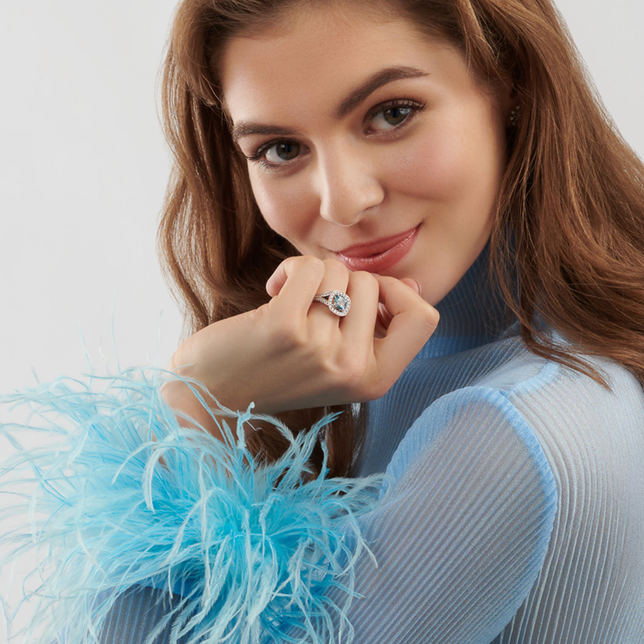 Model wearing a handcrafted 18ct white gold engagement  engagement ring featuengagement ring a large, cushion-cut blue aquamarine surrounded by a halo of small diamonds and smaller diamonds embedded along the band.