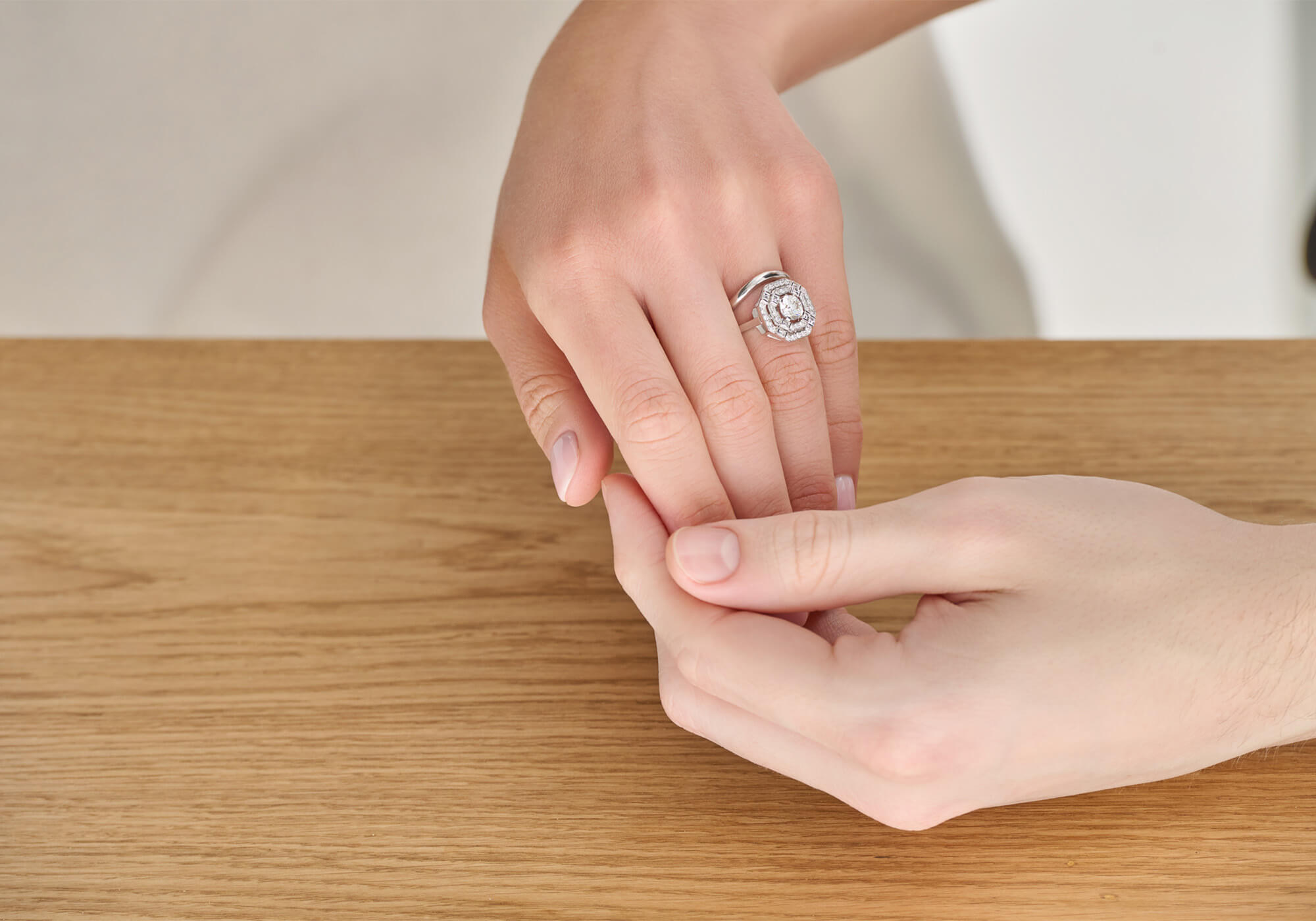 A woman's hand resting in a man's hand, showcasing an 18ct white gold engagement ring adorned with precious stones.