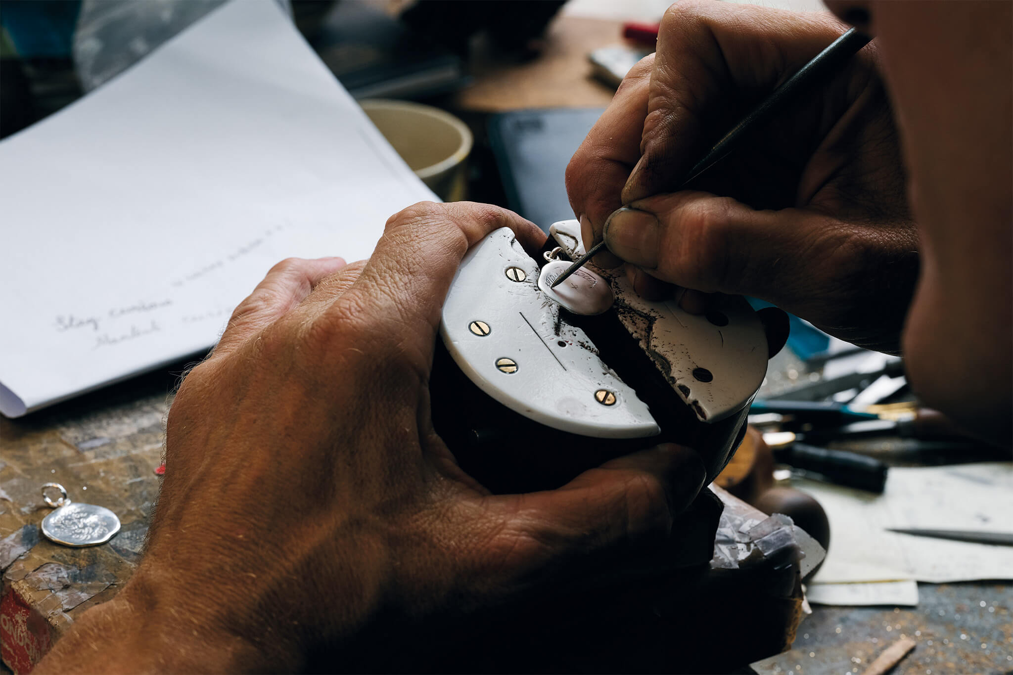 Craftsman hand engraving a silver necklace pendant in a London workshop.