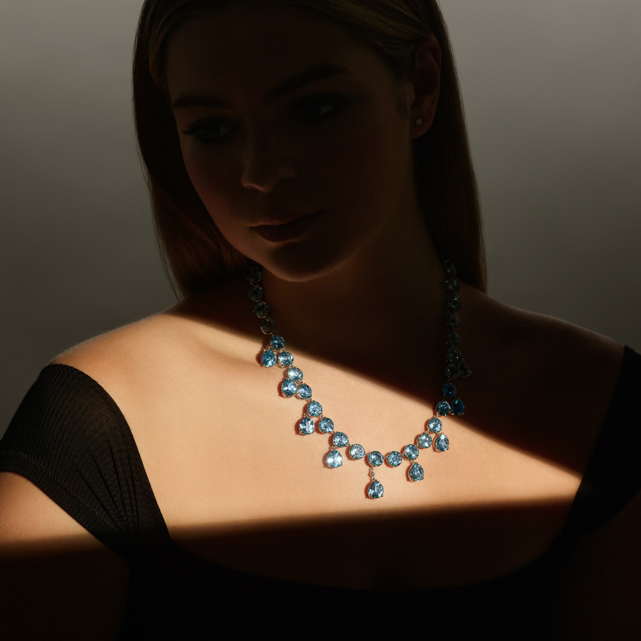 Model wearing a handcrafted white gold necklace featuring circular and drop blue topaz gemstones.
