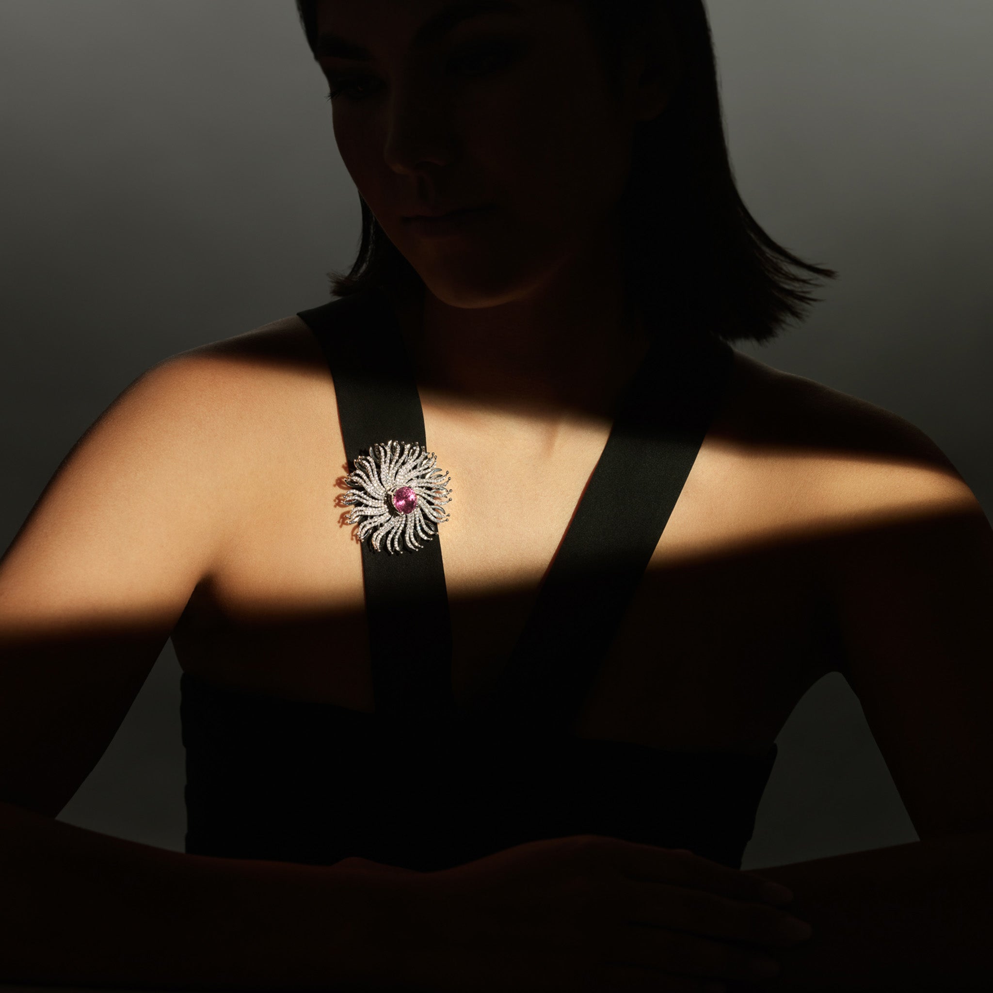 Model wearing a handcrafted 18ct white gold necklace pendant featuring a spider web shape of diamonds with a central pink tourmaline.
