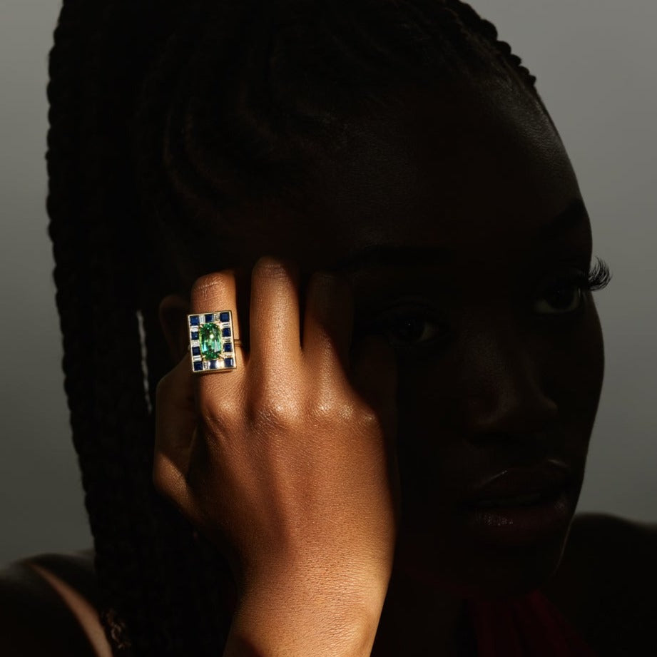 Model wearing a handcrafted 18ct yellow gold ring featuring a rectangular shape with a tourmaline surrounded by square sapphires and diamonds.