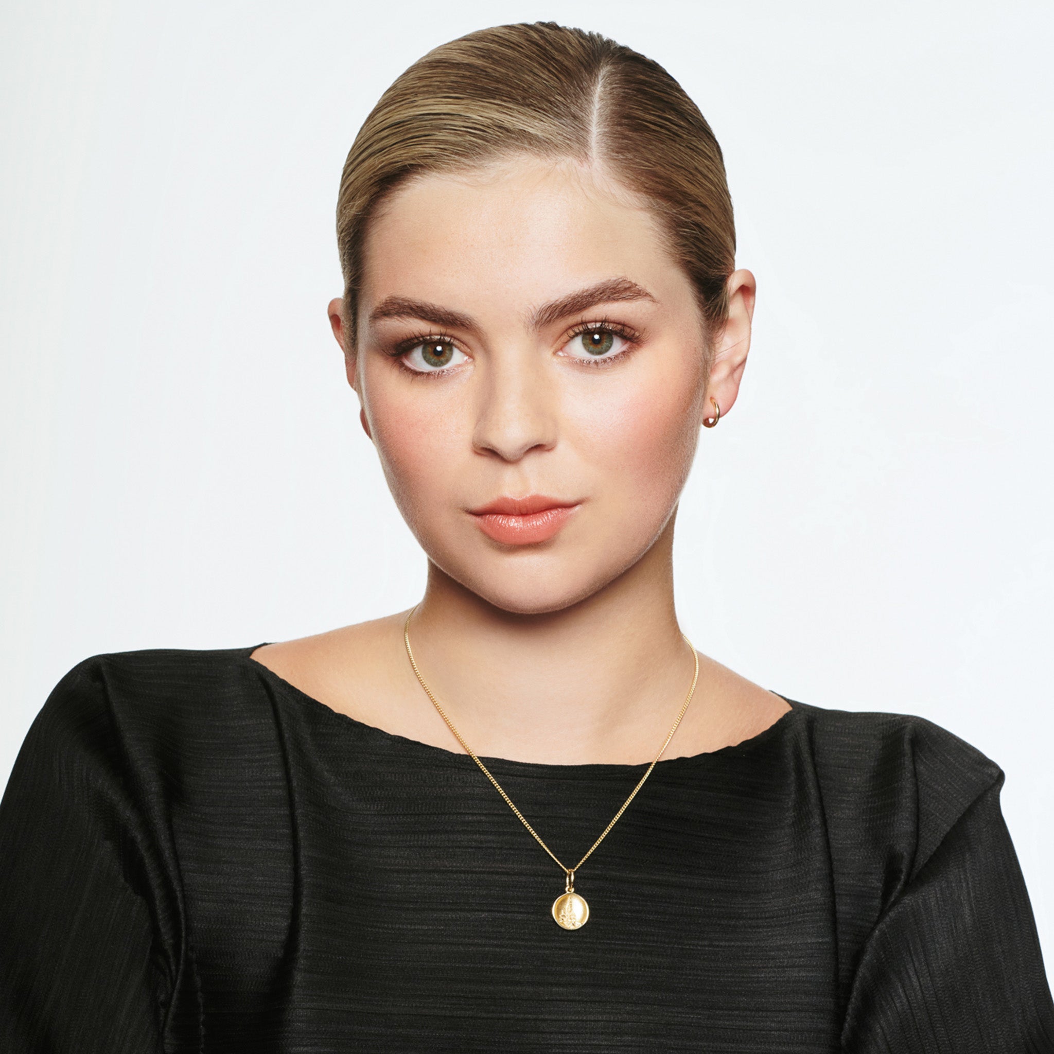 Model wearing a handcrafted round yellow gold necklace pendant 'en relief' with a flower.