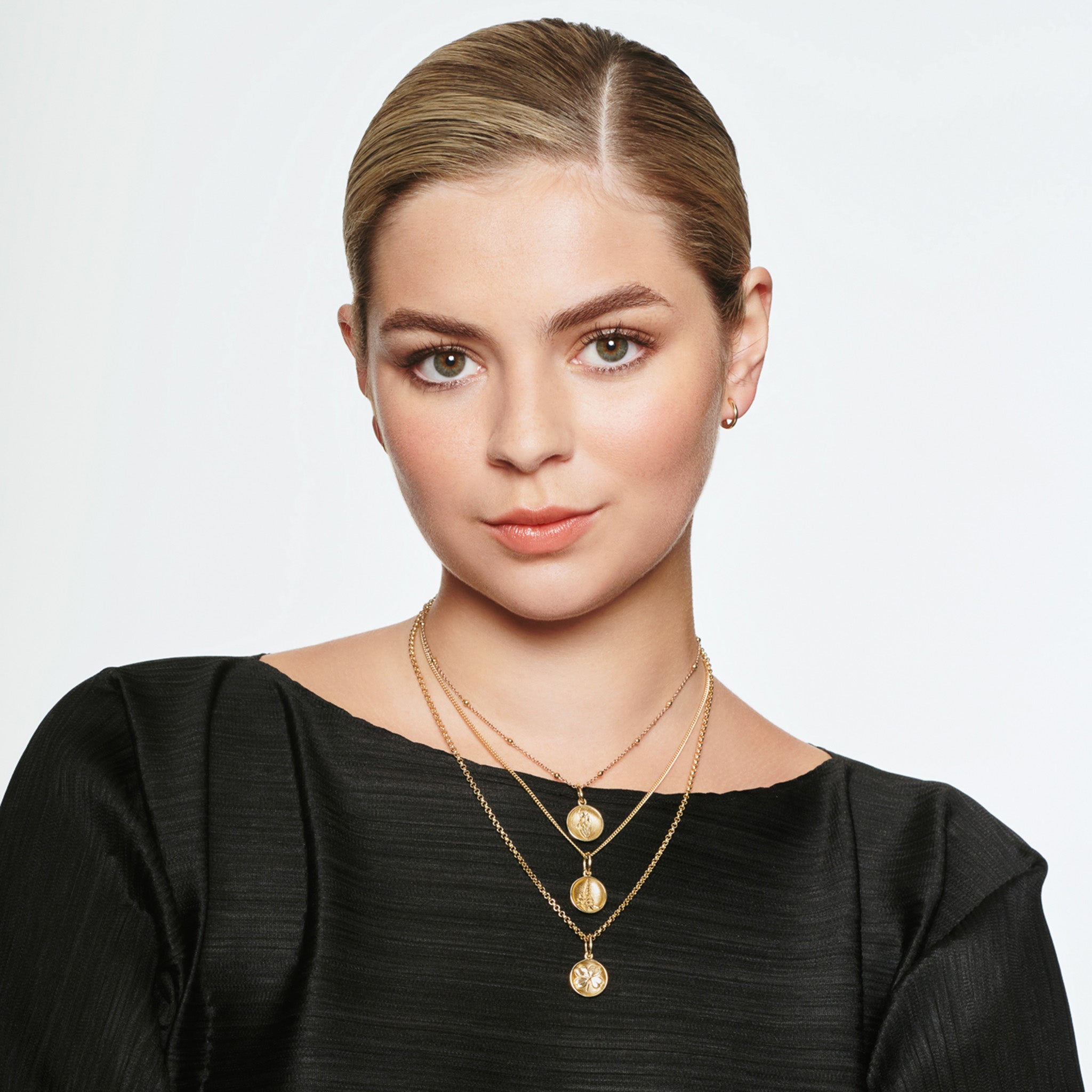 Model wearing a handcrafted round yellow gold necklace pendant featuring an engraving of Mont Saint-Michel Abbey in France on a chain along with two other pendant necklaces in gold.