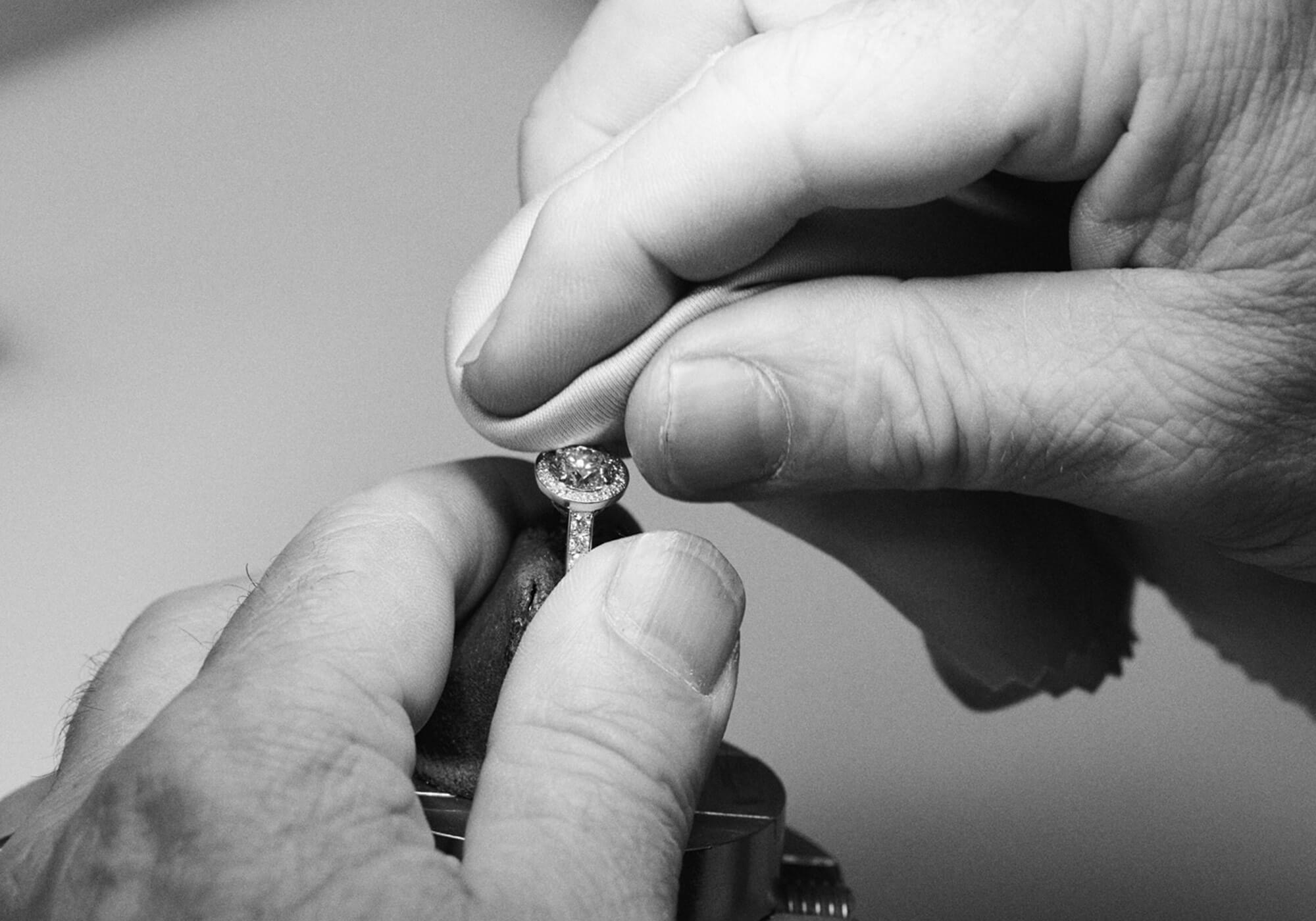 A black and white image of a platinum engagement ring with a central diamond surrounded by diamond pave, being carefully cleaned.