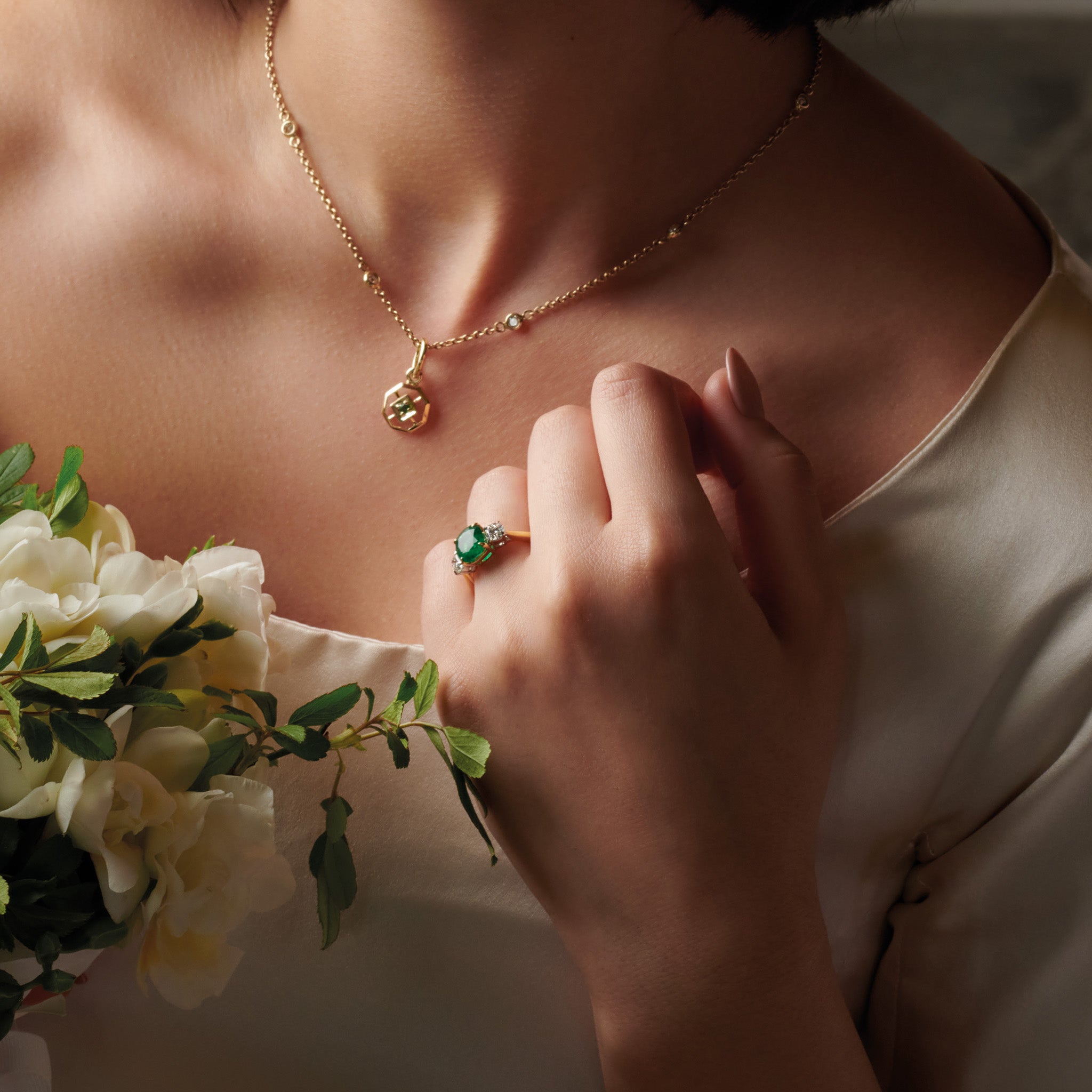 Model wearing a handcrafted 18ct yellow gold engagement ring featuring a large, cushion cut emerald at its center, surrounded by two smaller teardrop-shaped white diamonds.