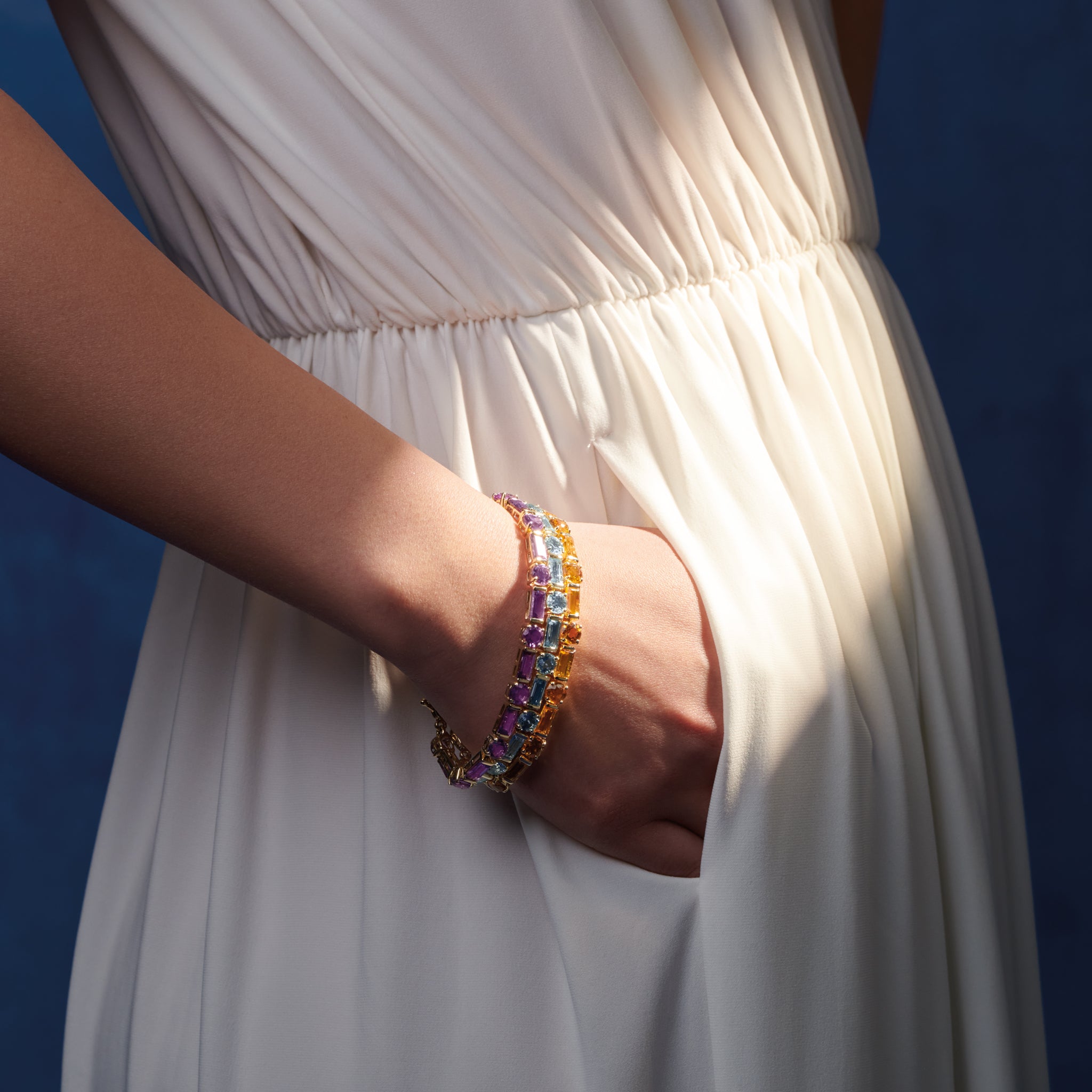 Model wearing three handcrafted yellow gold bracelets with baguette cut precious gemstones. 
