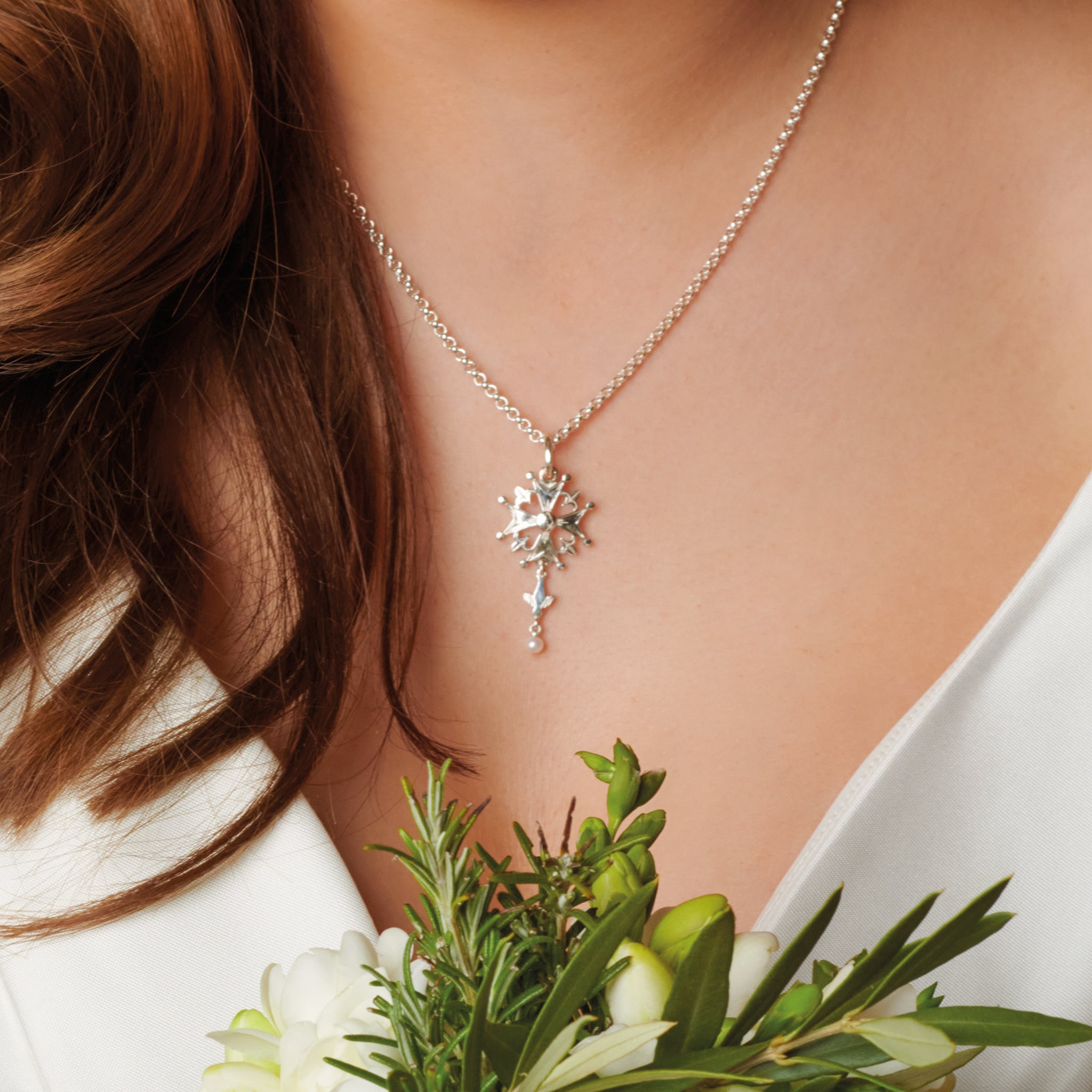 Model wearing a handcrafted sterling silver Huguenot cross pendant with pearl, birthstone of June.