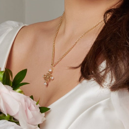 Model wearing a handcrafted cross necklace pendant in yellow gold with a symmetrical arrangement of pearls. 