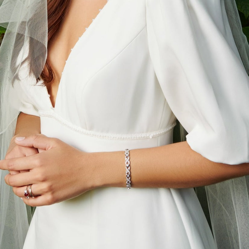 Model wearing a handcrafted 18ct white gold bracelet with a looping pattern, set with round cut diamonds. 
