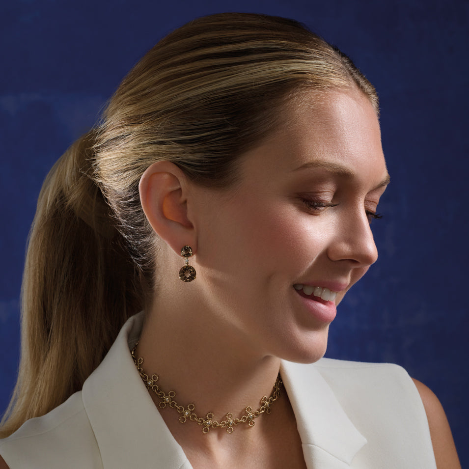 Model wearing handcrafted yellow gold earrings featuring circular smoky quartz gemstones and diamonds.
