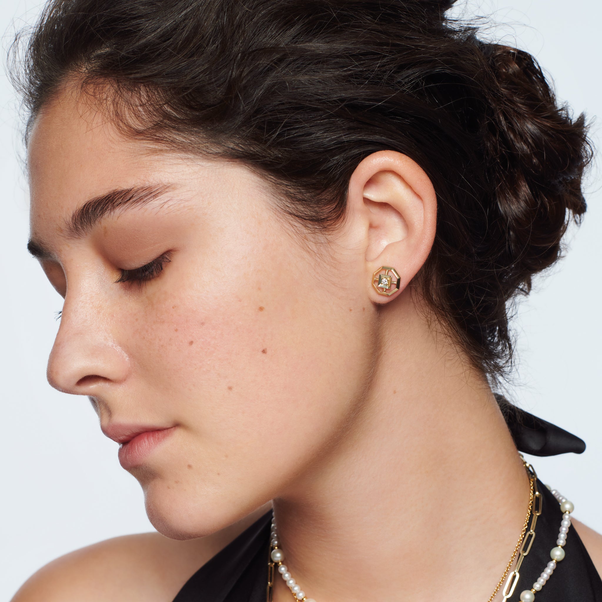 Model wearing handcrafted stud earrings featuring an octagonal design with a central precious stone. 