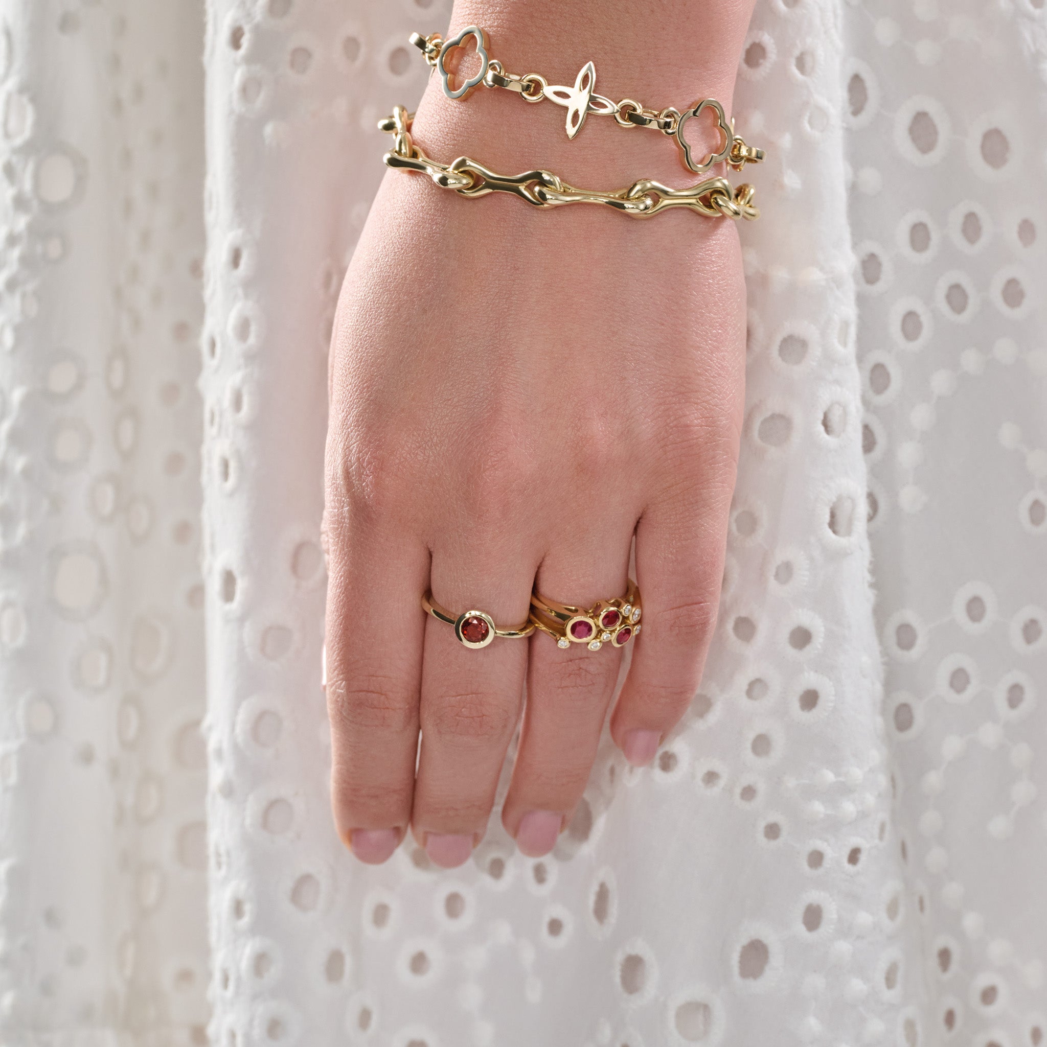 Model wearing a handcrafted 18ct yellow gold ring featuring different sized round rubies and diamonds and a yellow gold bracelet featuring bone-like links. 
