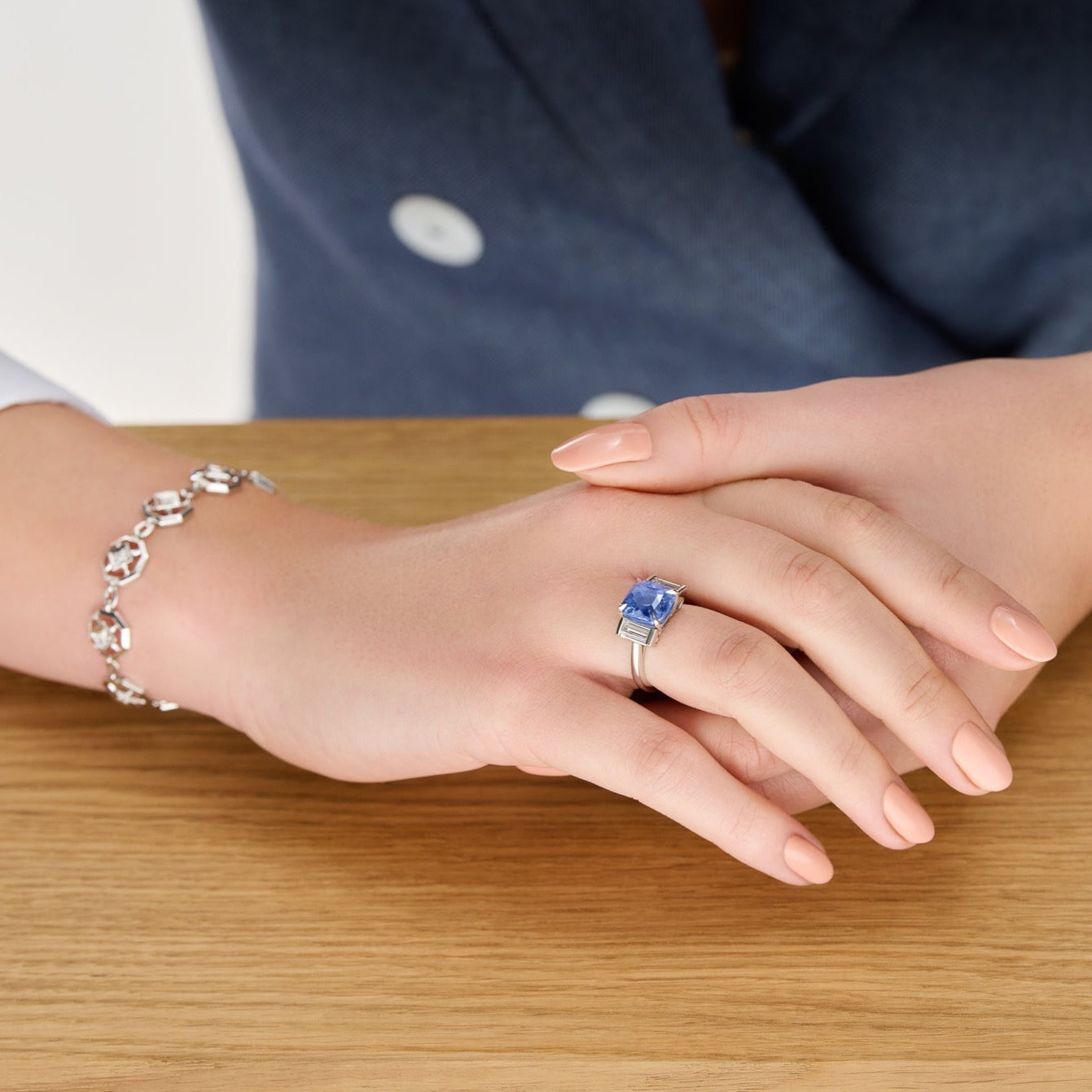 Model wearing a handcrafted platinum engagement ring featuring a central rectangular blue sapphire flanked by two smaller rectangular diamonds on each side, all set in a sleek band.