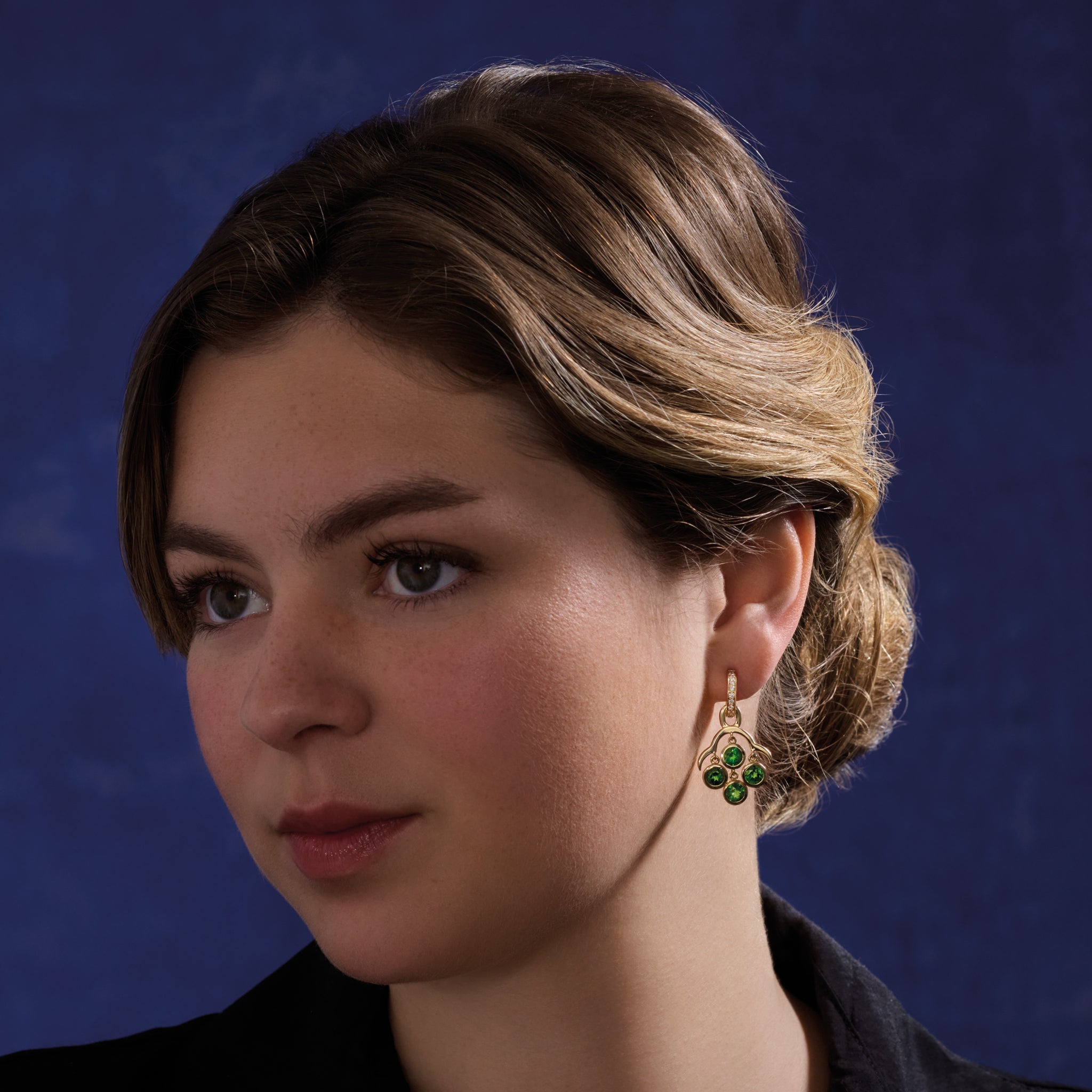 Model wearing handcrafted yellow gold earring drops inspired by acai berries featuring four chrome diopside gemstones.