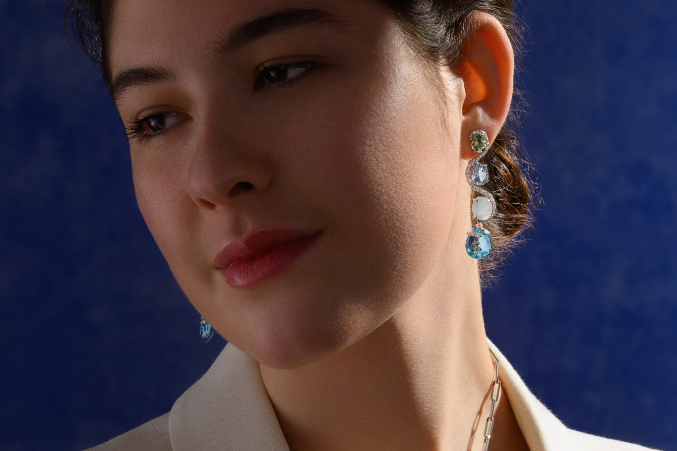 Model wearing handcrafted white gold earrings with blue topaz gemstones, birthstone of November.