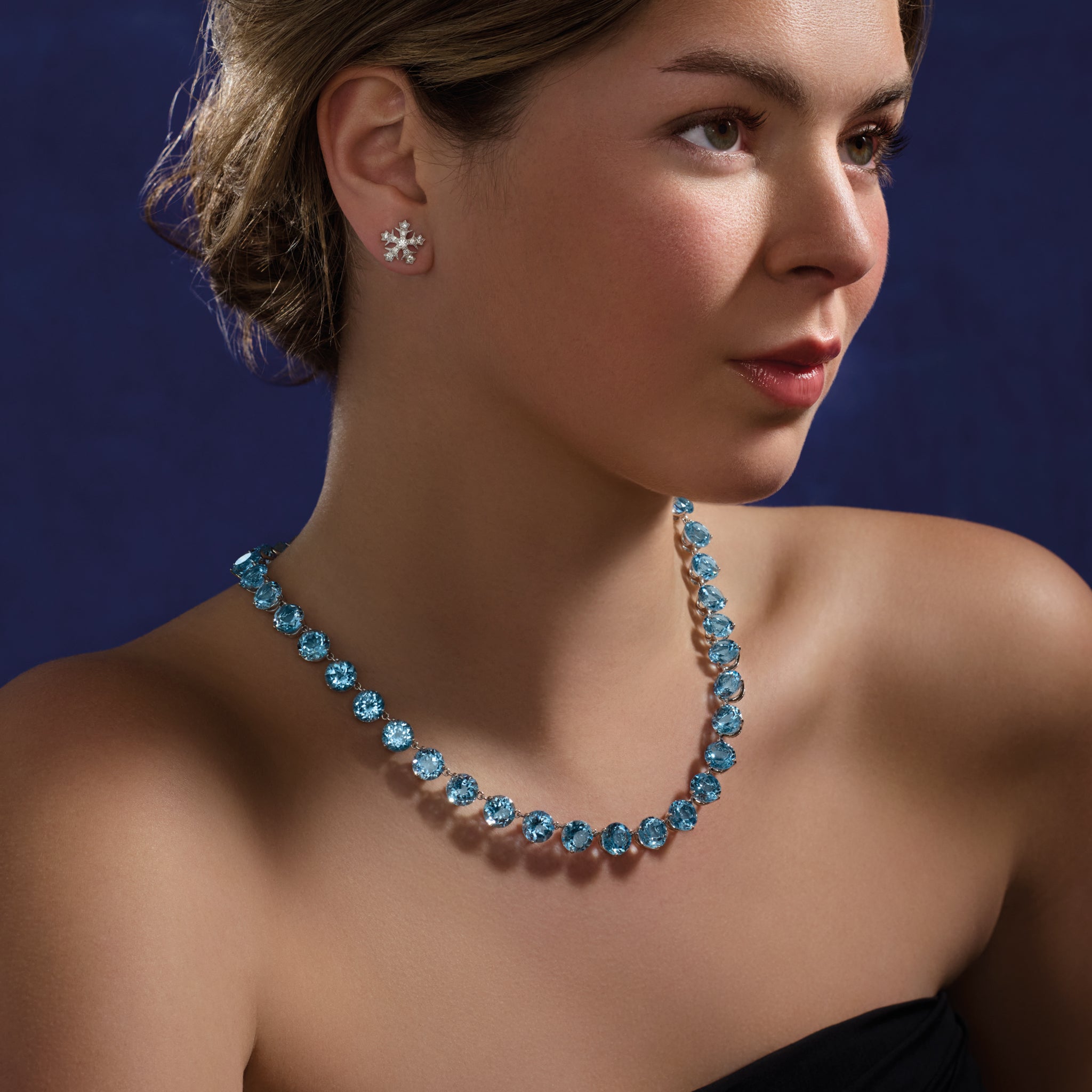 Model wearing a handcrafted white gold necklace featuring circular blue topaz gemstones.
