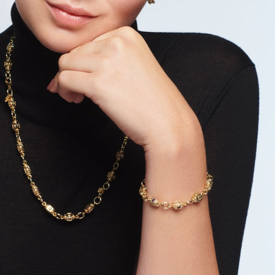 Model wearing a handcrafted yellow gold bracelet featuring a design of interlocking circles, each connected through intricately detailed set with the precious stones amethyst, peridot, garnet and aquamarine.