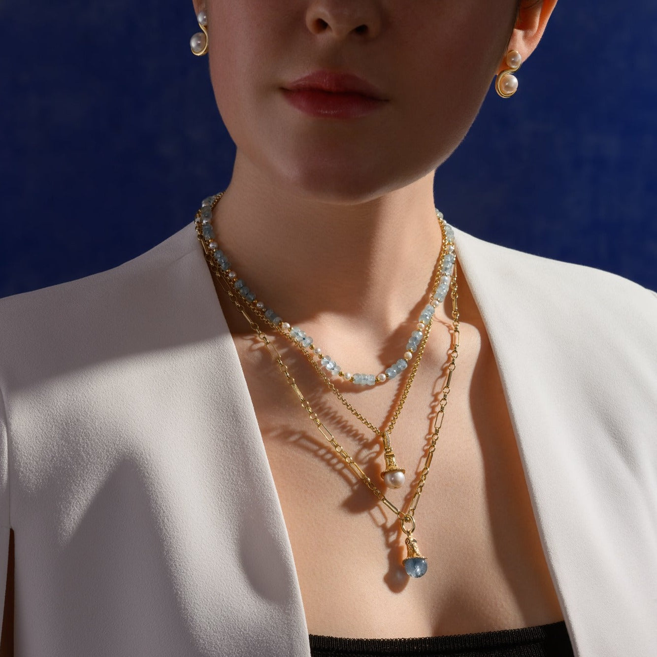 Model wearing handcrafted necklace pendants in precious metals with beads of precious stones.