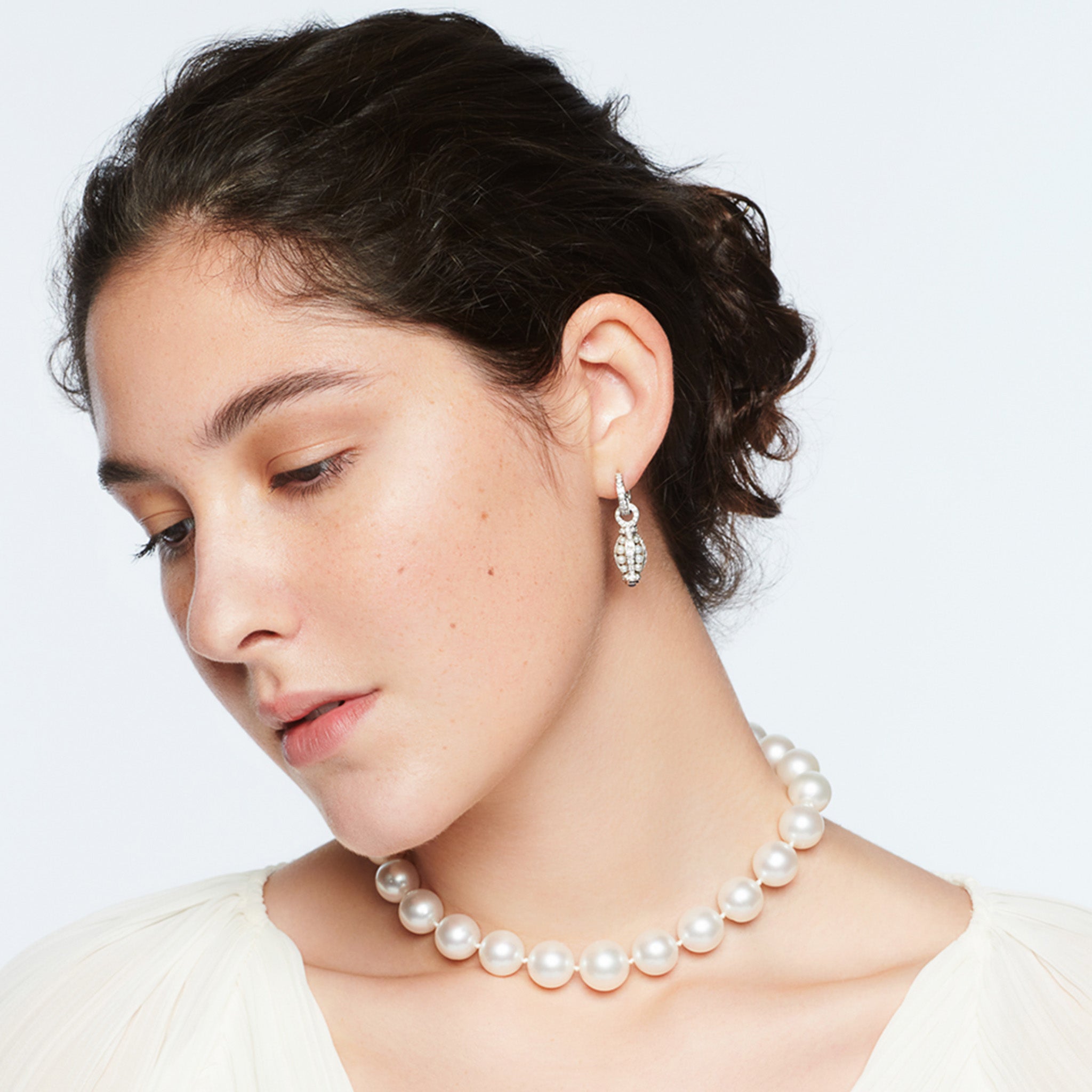 Model wearing handcrafted 18ct white gold teardrop shaped earring drops with pearls enclosed with diamonds and a precious gemstone at the bottom. 