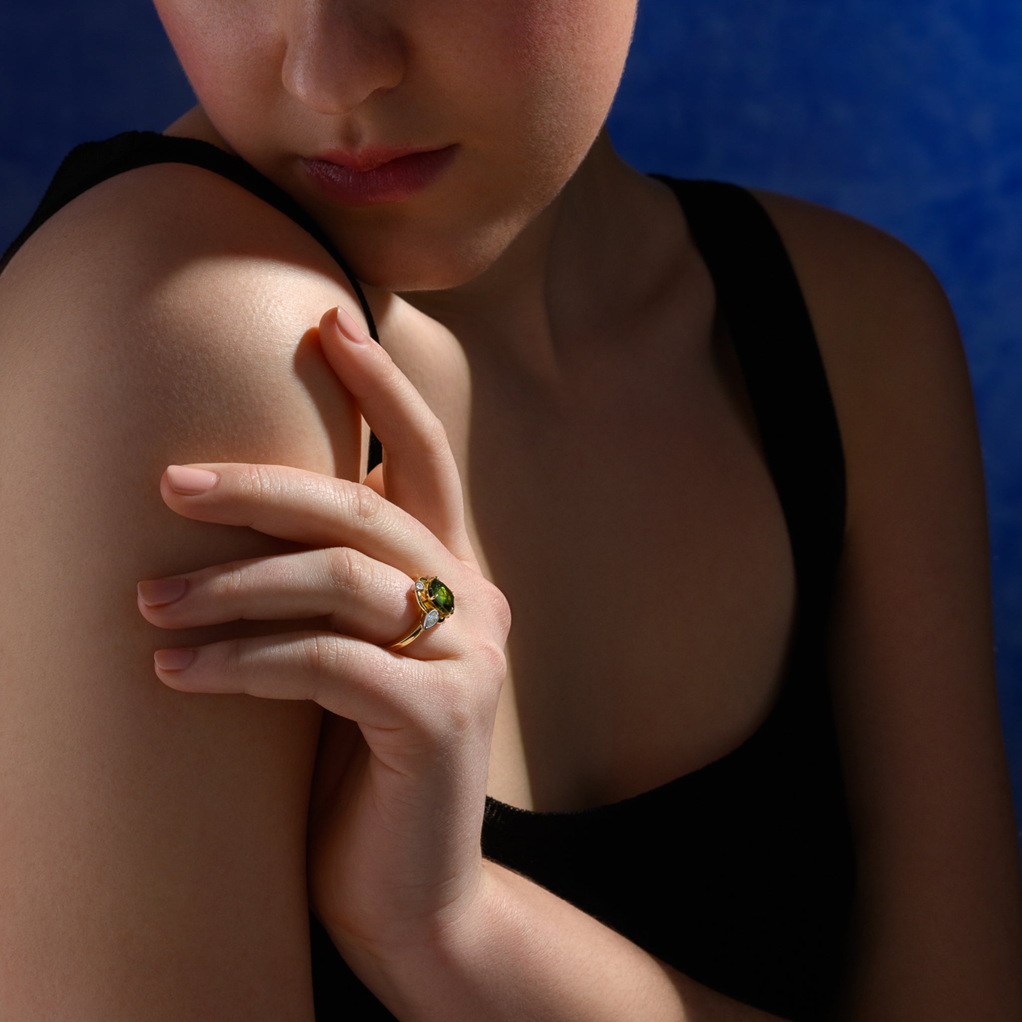 Model wearing handcrafted 18ct yellow gold engagement ring ring featuring a green tourmaline at its center, surrounded by four smaller diamonds, two teardrop-shaped.