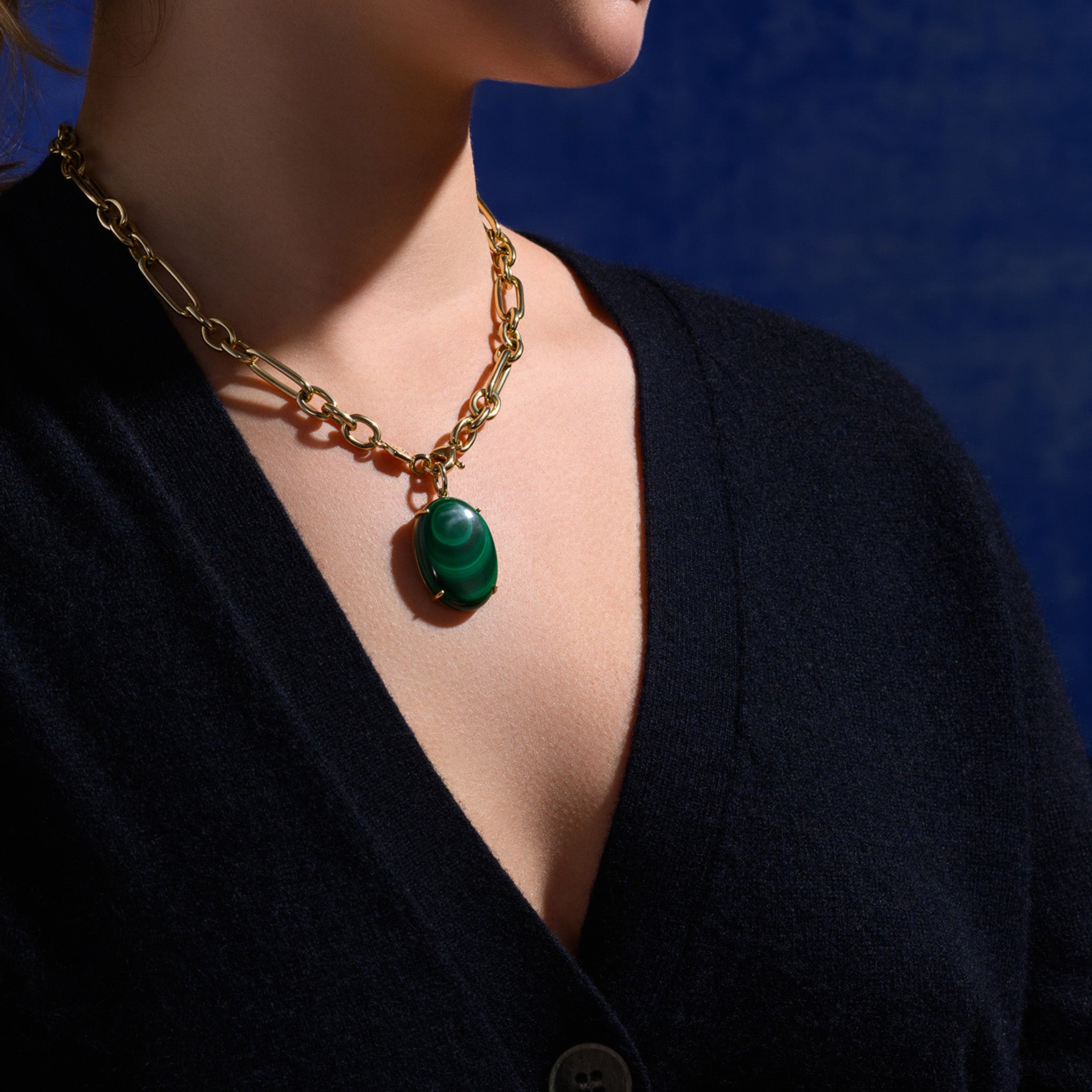 Model wearing a handcrafted yellow gold necklace pendant with a large round central malachite hanging from a gold chain. 