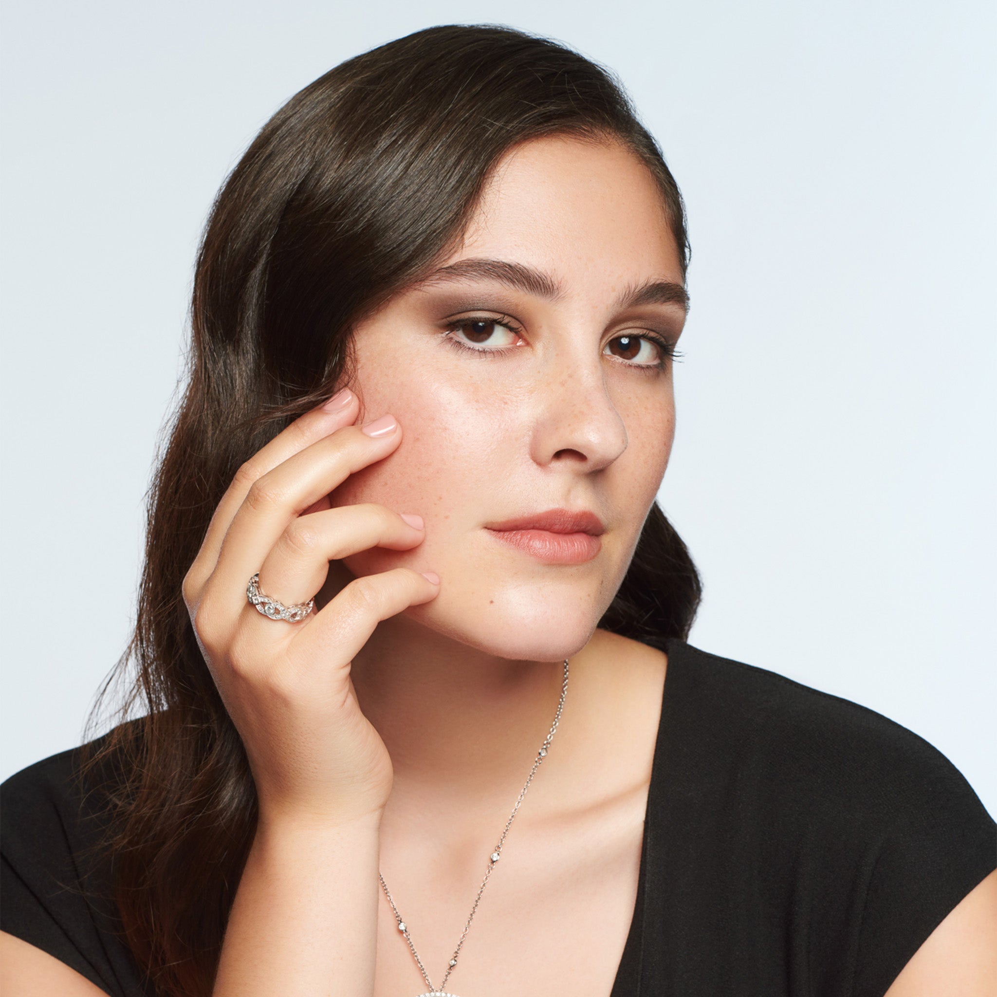 Model wearing a handcrafted 18ct white gold engagement engagement ring with a looping pattern, set with round-cut diamonds. 