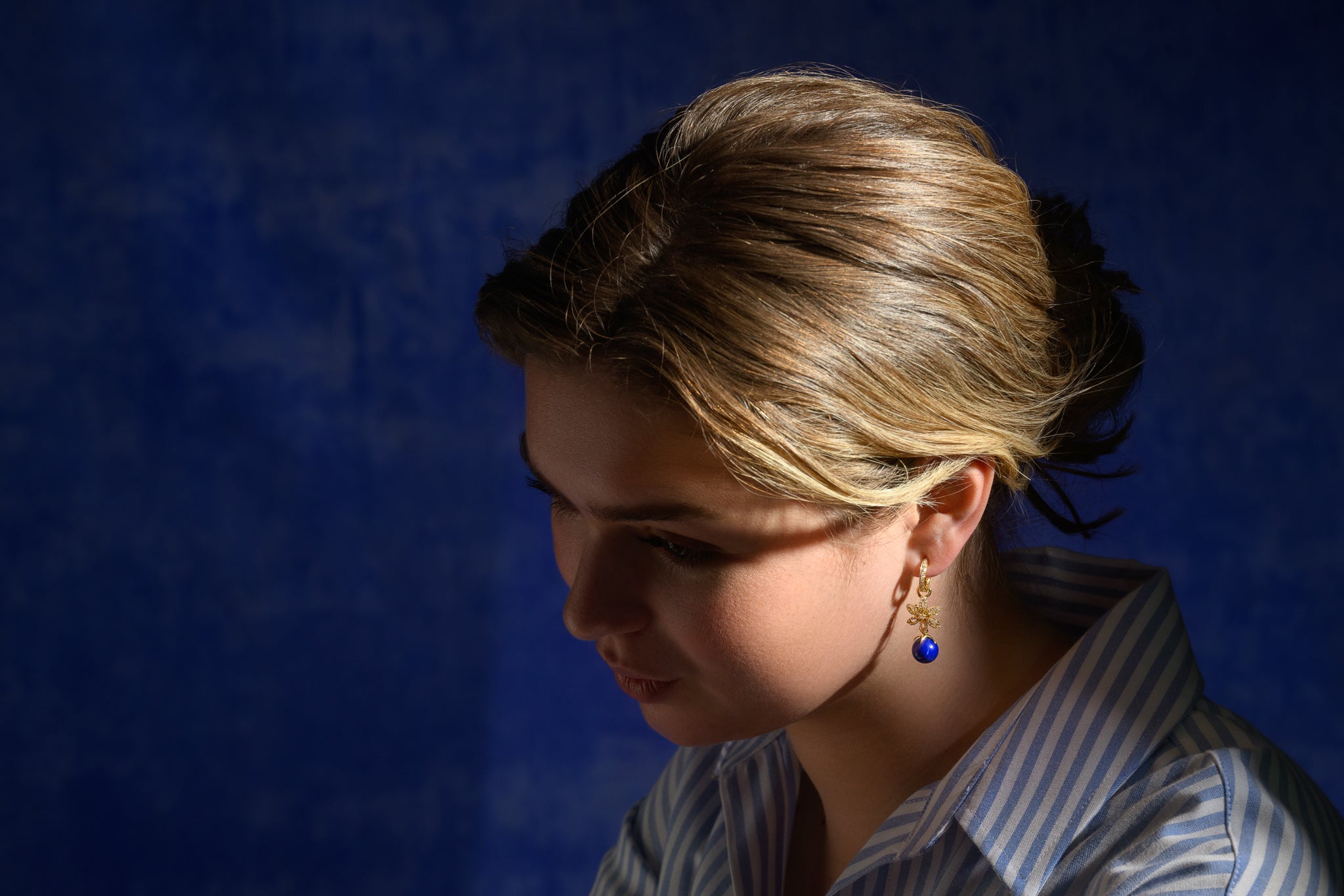 Model wearing handcrafted yellow gold earring drops featuring a lapis lazuli bead at the bottom.