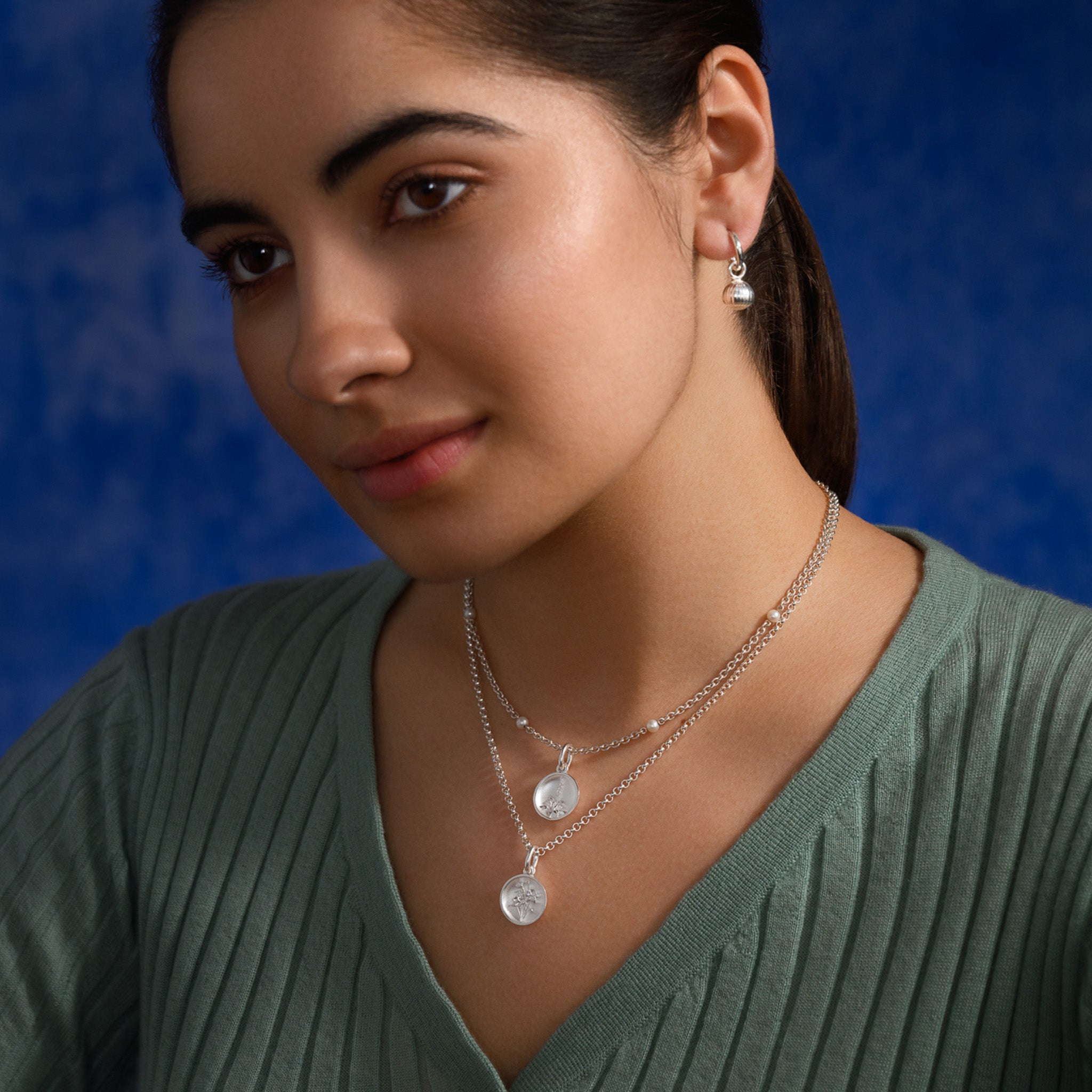 Model wearing a handcrafted round sterling silver necklace pendant featuring an 'en relief' flower.